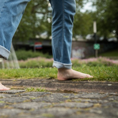 Eine Person geht barfuß in einem Park von einem Gehweg auf eine Wiese