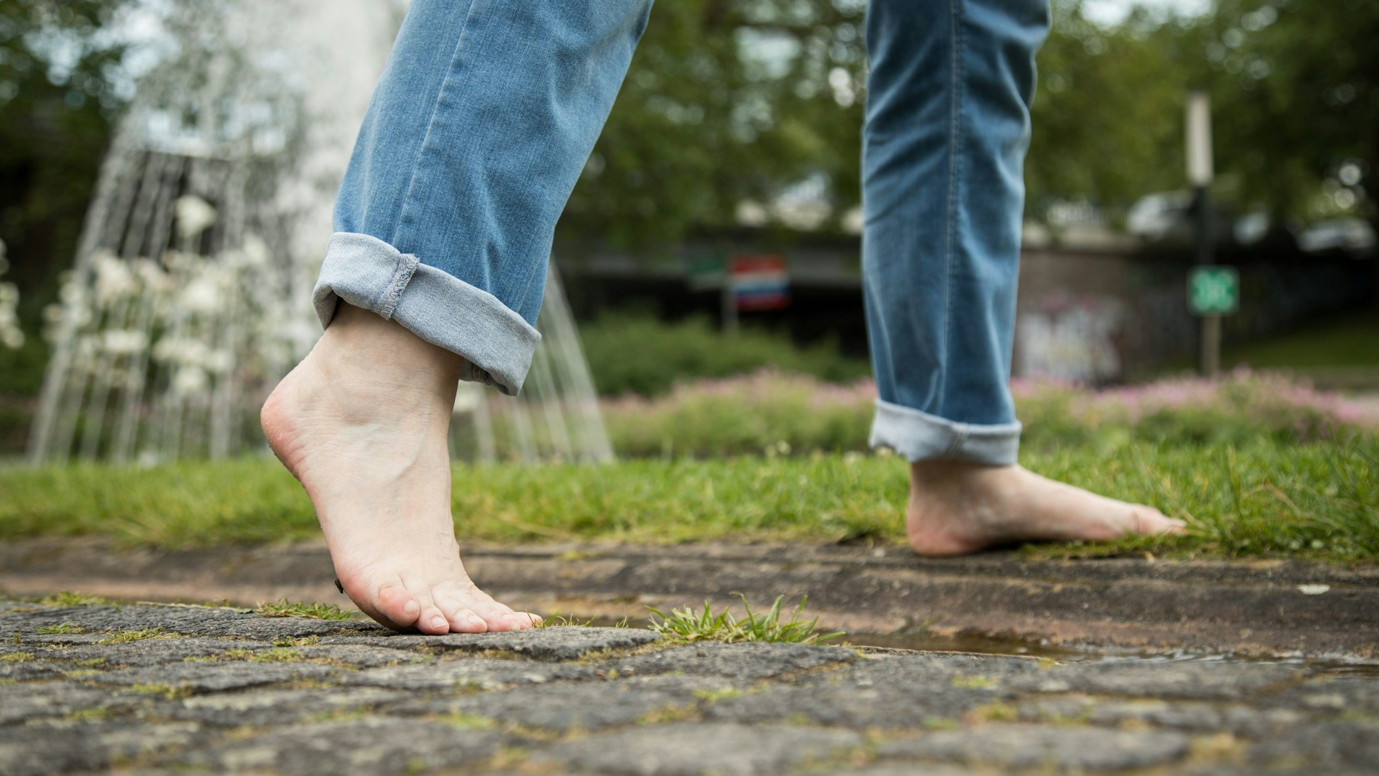 Eine Person geht barfuß in einem Park von einem Gehweg auf eine Wiese