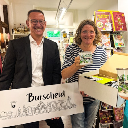 Neues Merchandise für Burscheid: Bürgermeister Drik Runge (v.l.) mit der Burscheid-Skyline, Buchhändlerin Ute Hentschel und Illustratorin Myria Stricker mit Burscheid-Emailletassen.