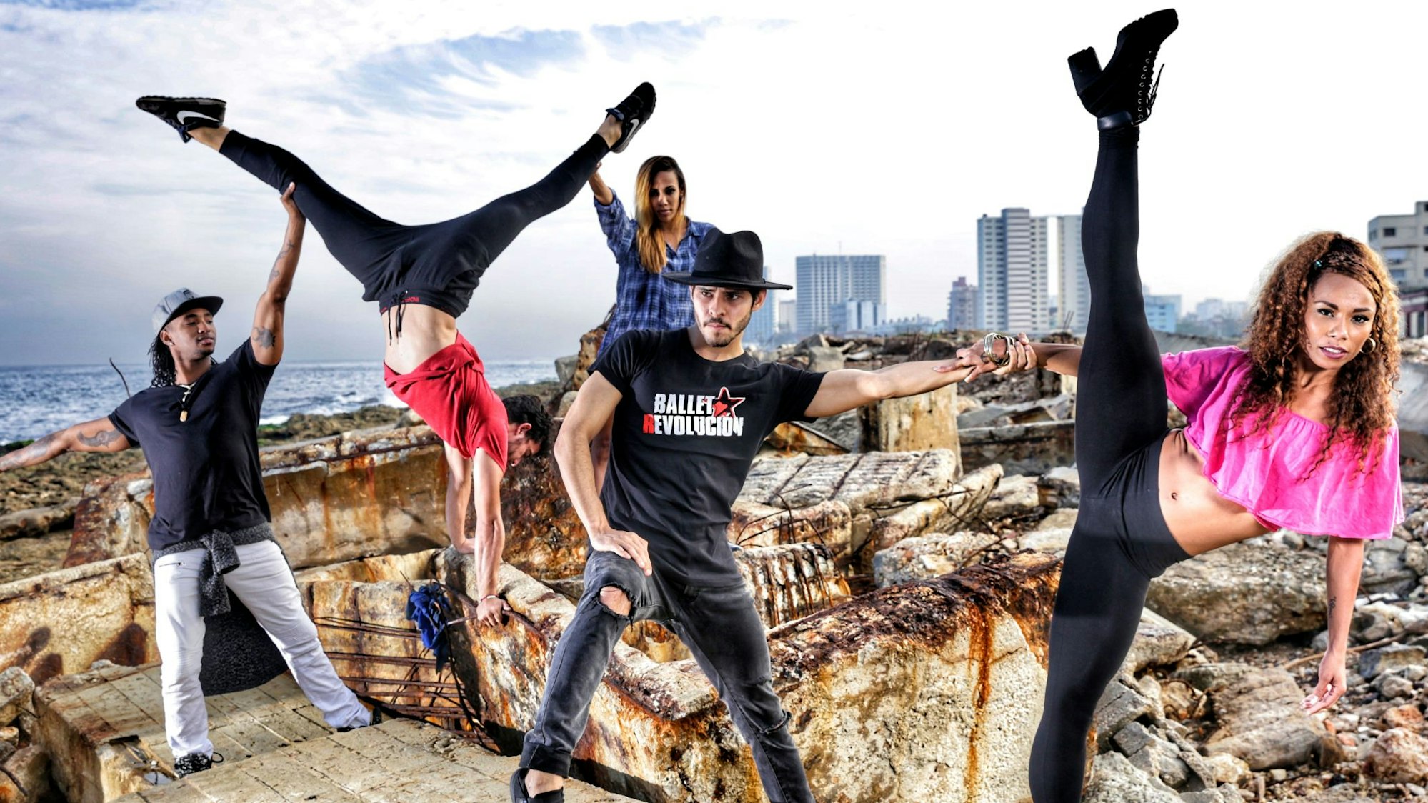 Zu sehen ist die Gruppe „Ballet Revolucion“. Im Hintergund zu sehen sind ein Ozean, Hochhäuser und Felsen.