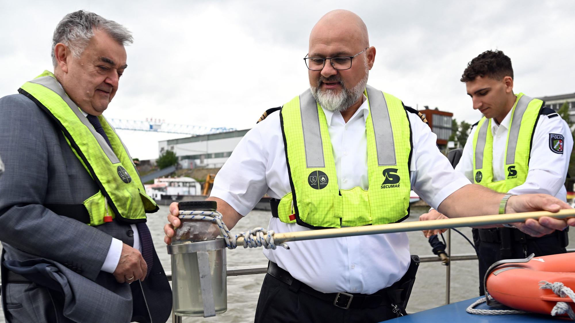 Axel Scholl (M), Hauptkommissar, zeigt auf dem Wasserschutzboot WSP 1 auf dem Rhein Herbert Reul (CDU,l) eine Wasserprobe die er mit Valentino West (r), Kommissaranwärter, genommen hat.