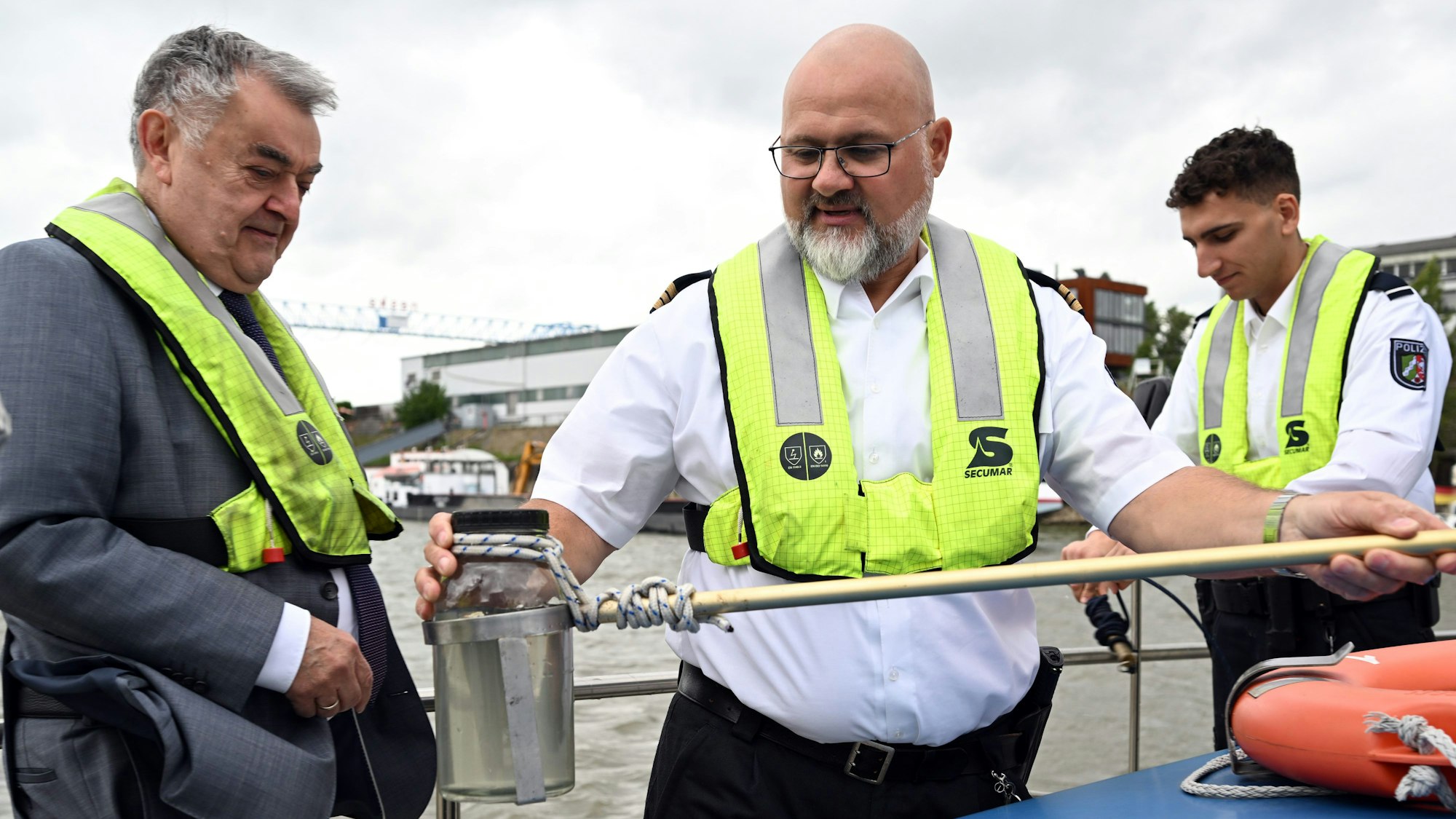 Axel Scholl (M), Hauptkommissar, zeigt auf dem Wasserschutzboot WSP 1 auf dem Rhein Herbert Reul (CDU,l) eine Wasserprobe die er mit Valentino West (r), Kommissaranwärter, genommen hat.