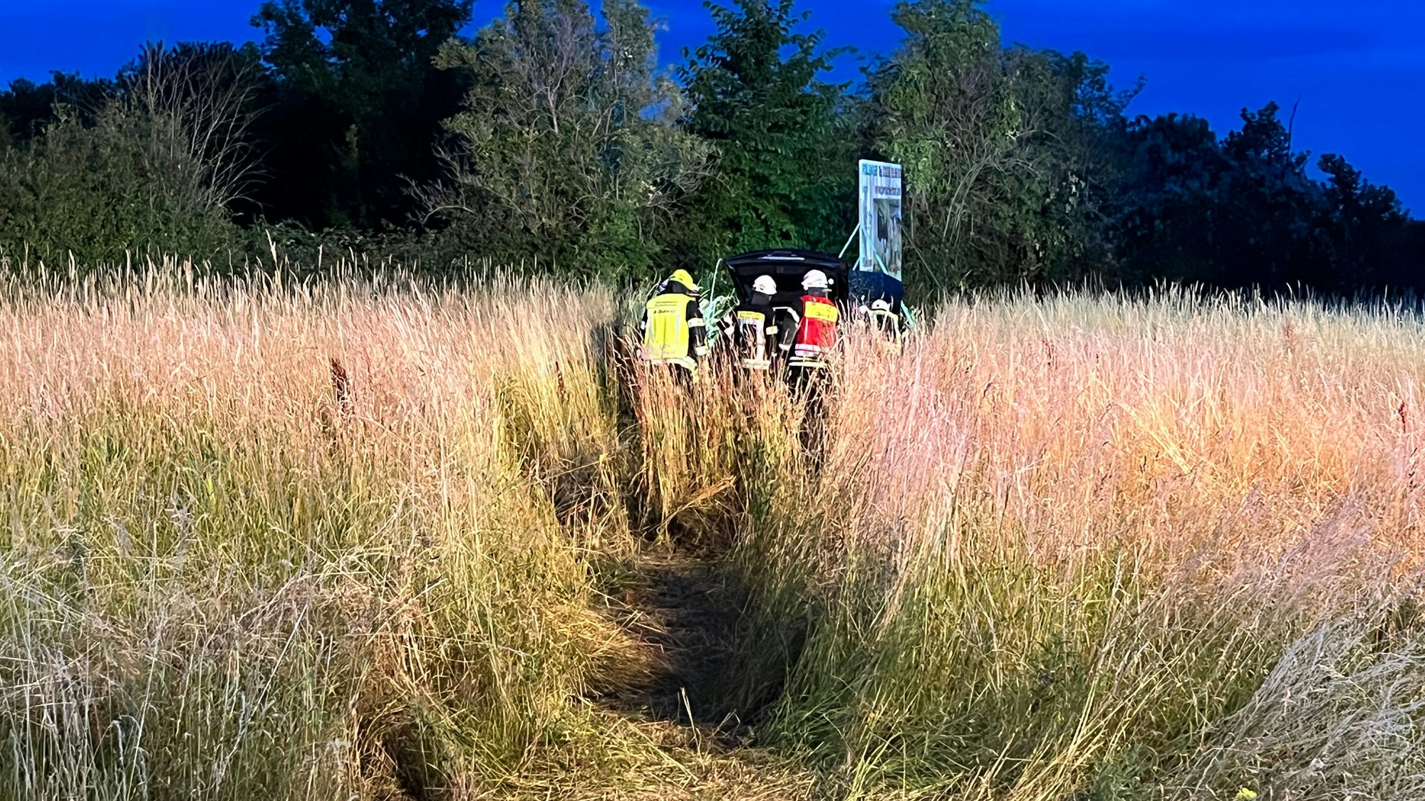 Die Einsatzkräfte im Feld vor dem Anhänger mit Werbetafel.