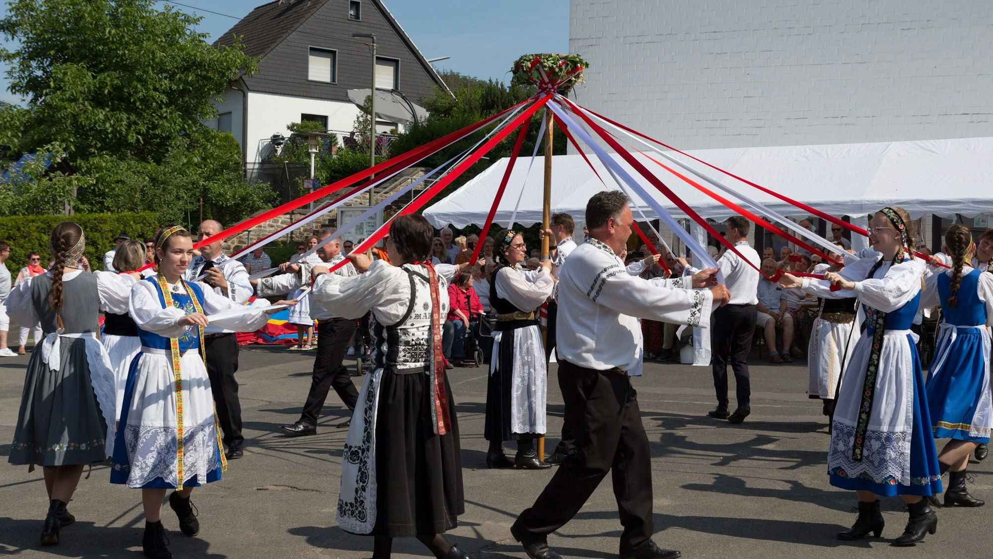 Männer und Frauen in bunten Trachten tanzen mit Bändern im Kreis.