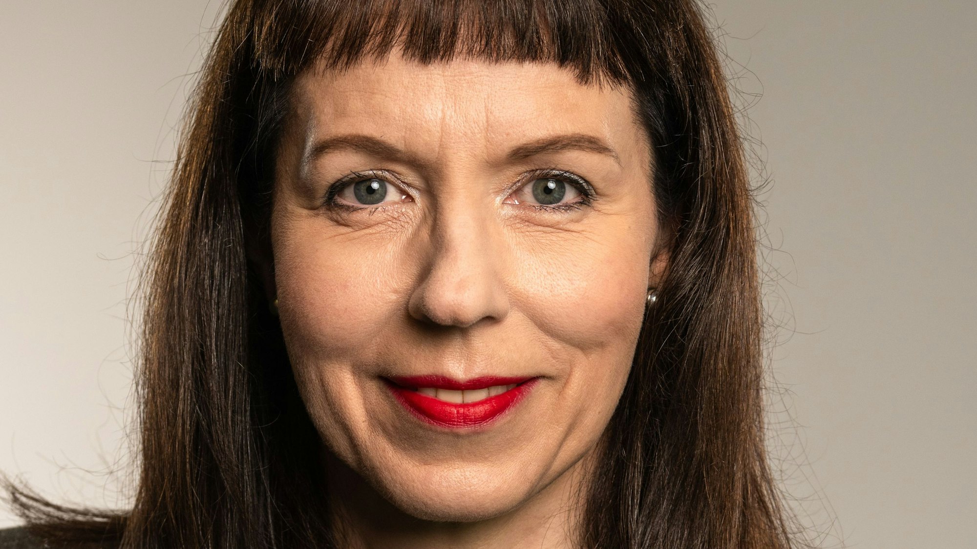 Ein Porträtfoto von Gisela Eichler. Sie hat schulterlange dunkle Haare mit Pony, trägt roten Lippenstift und guckt freundlich.