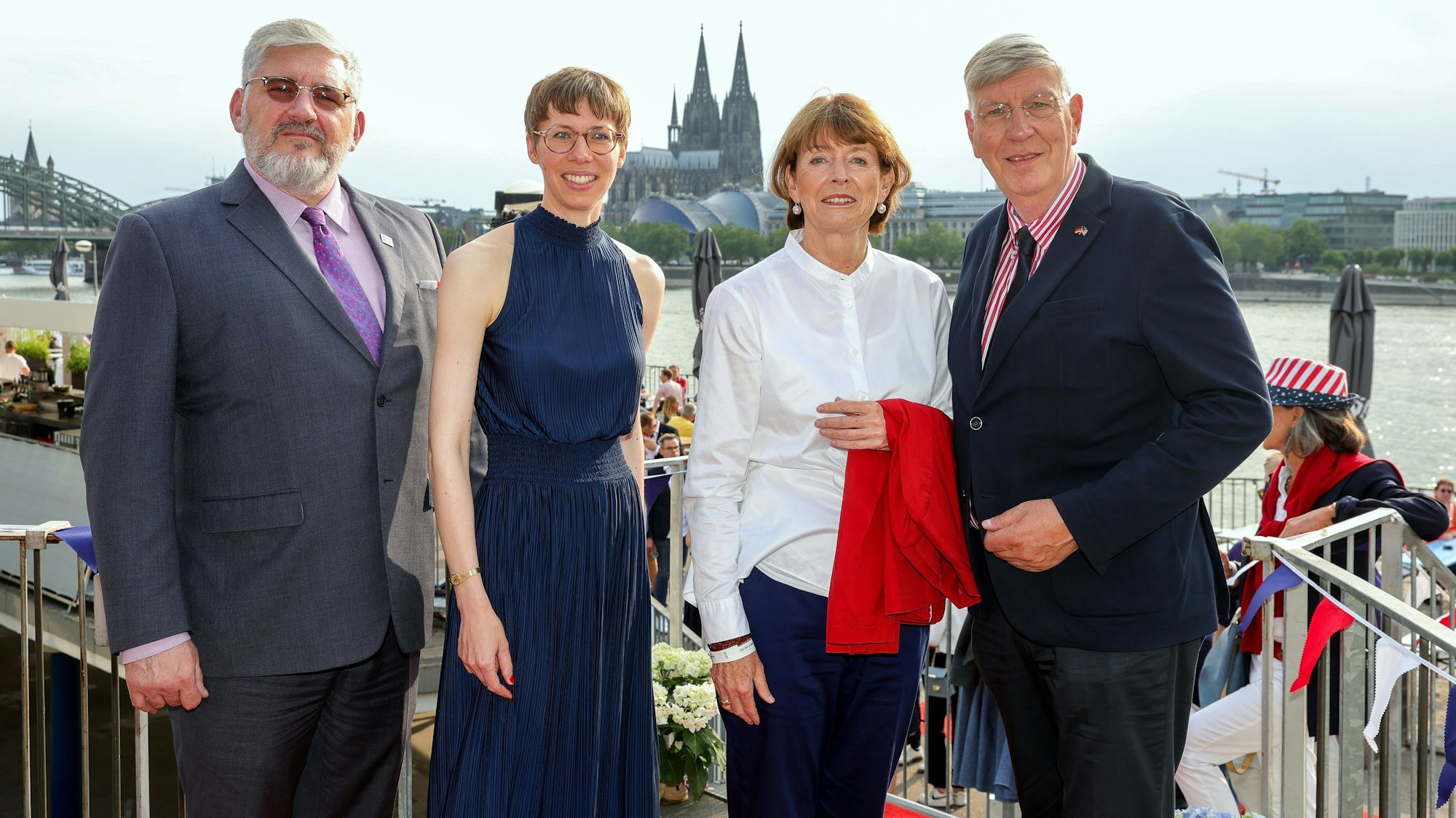 Auf dem Bild stehen vier Personen auf den Rheinterrassen. Sie sind blau, weiß und rot gekleidet und im Hintergrund sieht man den Kölner Dom.