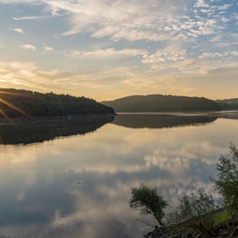 Die Sonne steht über den Bäumen am Ufer der Großen Dhünn-Talsperre.
