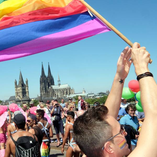 Jemand schwingt eine Regenbogenflagge. Im Hintergrund ist der Kölner Dom zusehen.