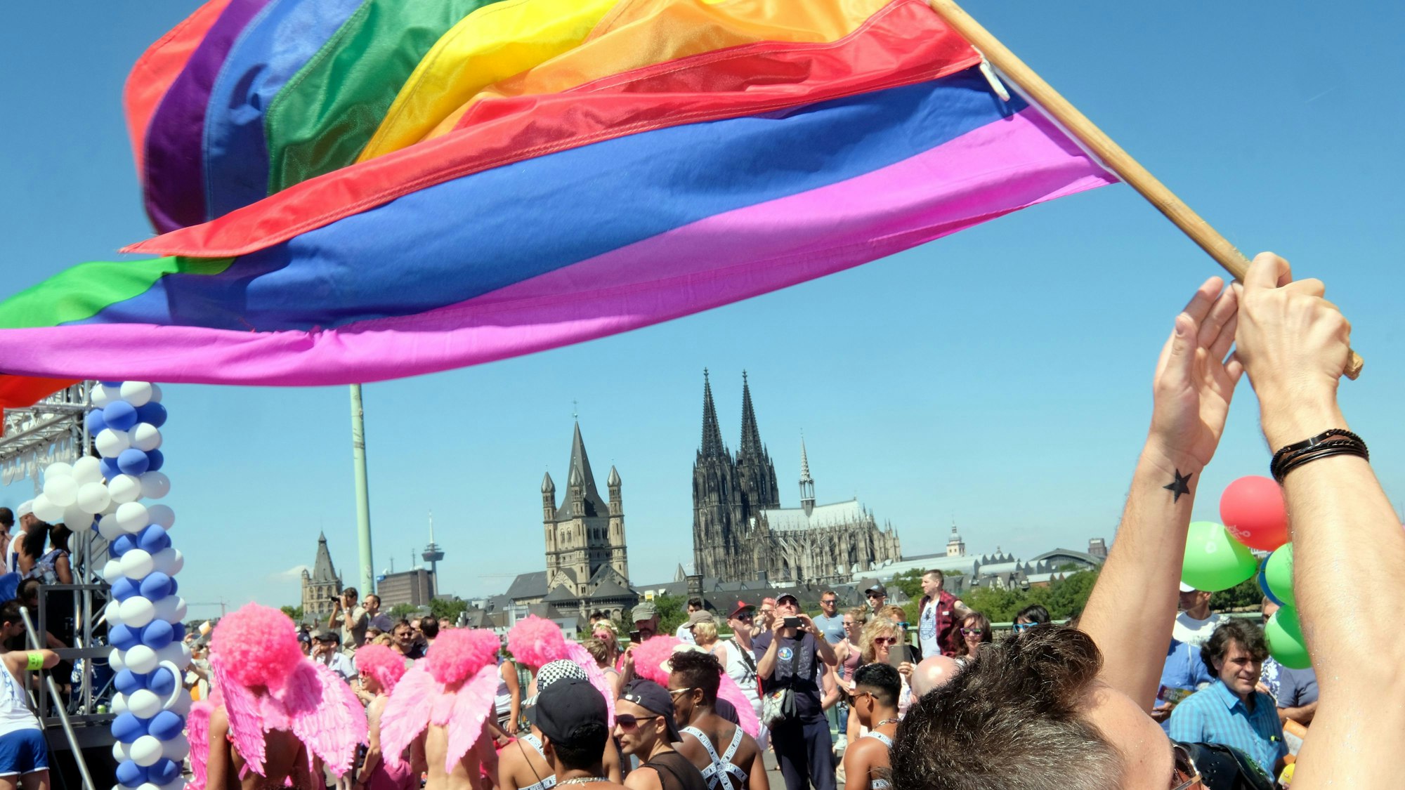 Jemand schwingt eine Regenbogenflagge. Im Hintergrund ist der Kölner Dom zusehen.