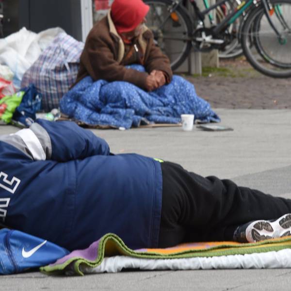 Das Foto zeigt einen obdachlosen Menschen, der auf dem Asphalt liegt.