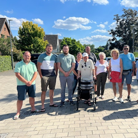 Mehrere Menschen stehen nebeneinander auf einer Straße.