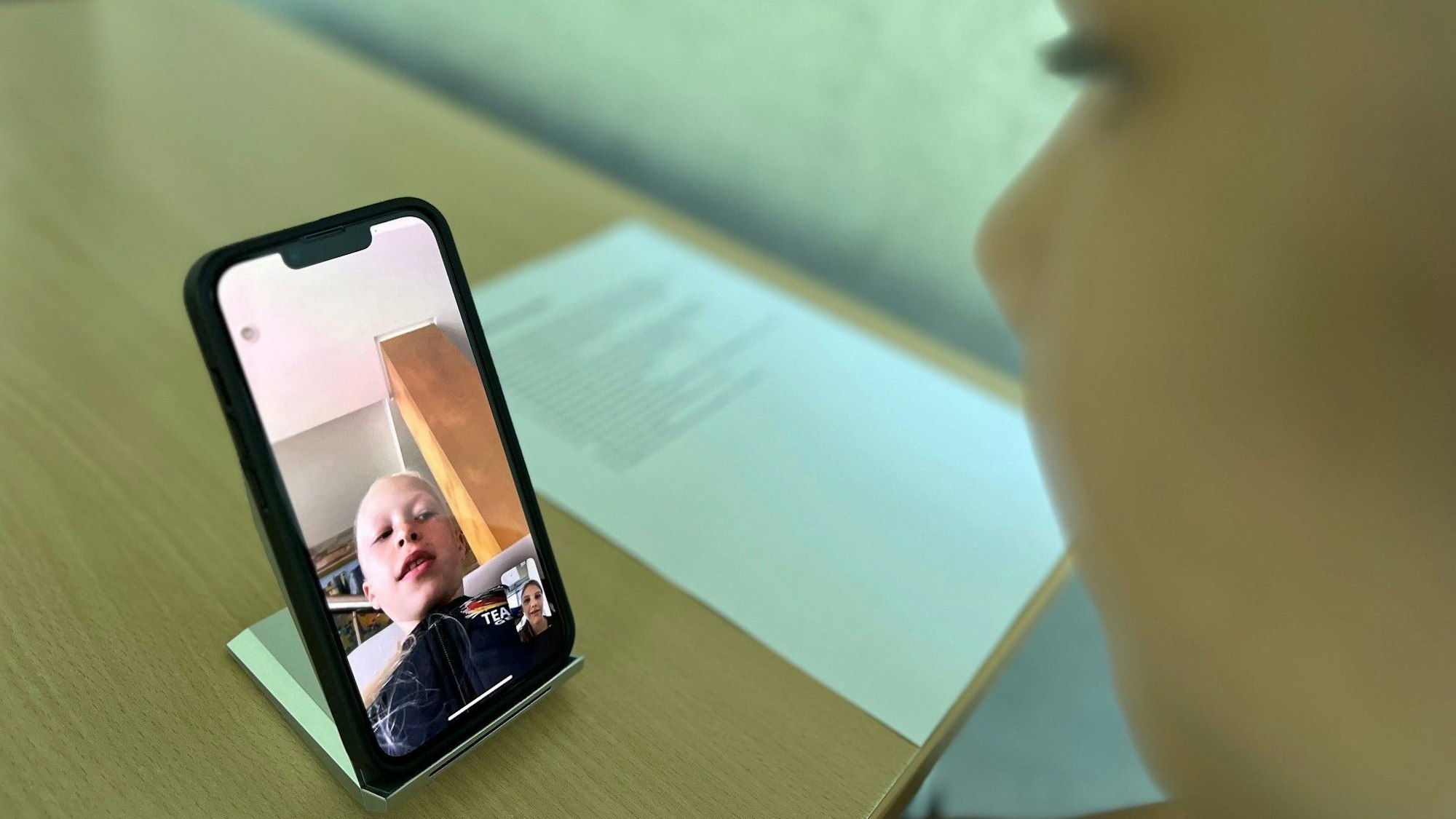 Emilia interviewt Maja per Videotelefonat über ein Handy, das vor ihr auf dem Tisch steht