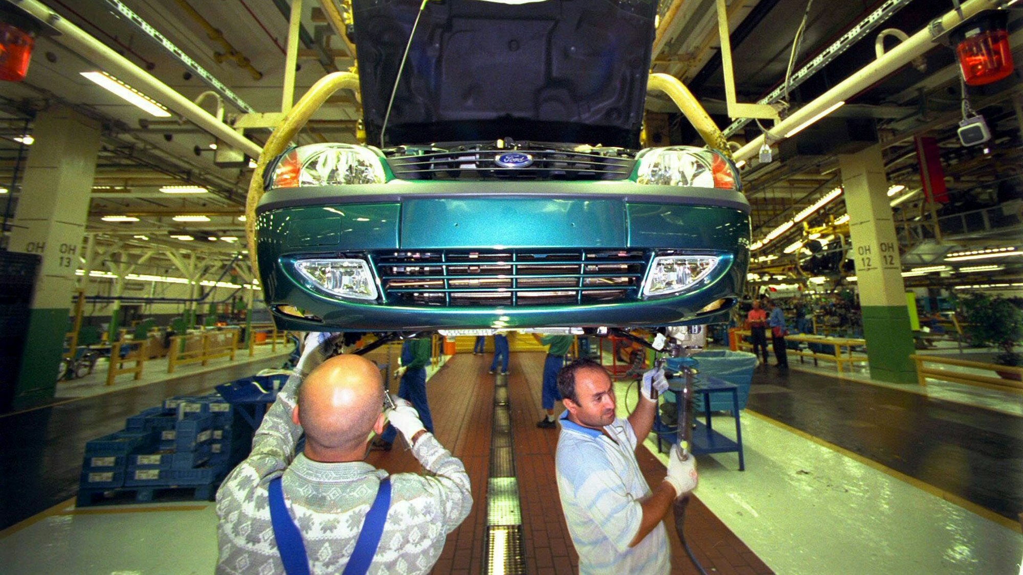 Endmontage eines Ford Fiesta in Köln-Niehl im Jahr 1999: zwei Automonteure arbeiten unter einem türkisen Fiesta in einer Produktionshalle.