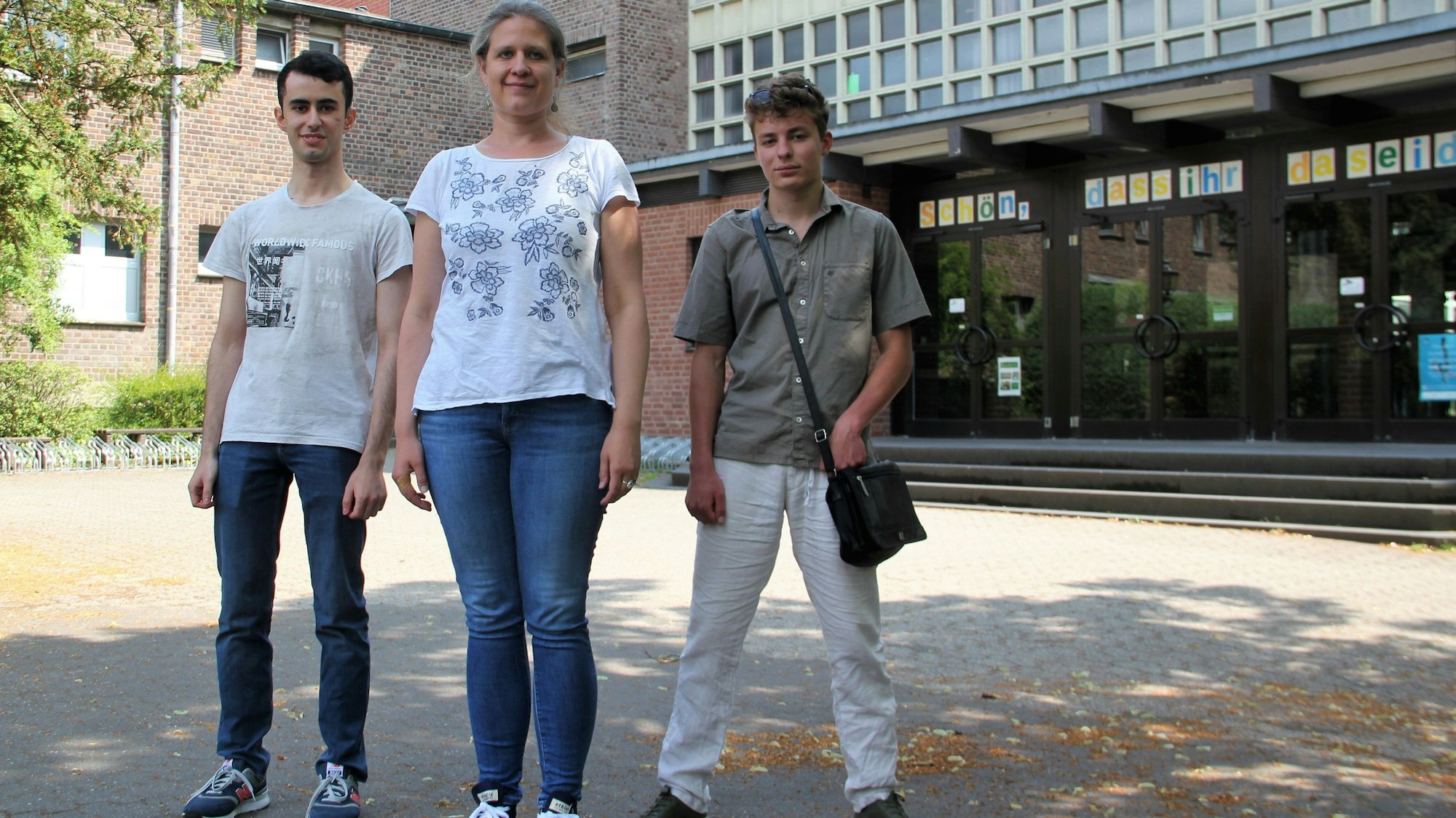 Zwei junge Männer stehen links und rechts von einer blonden Frau mit Pferdeschwanz.
