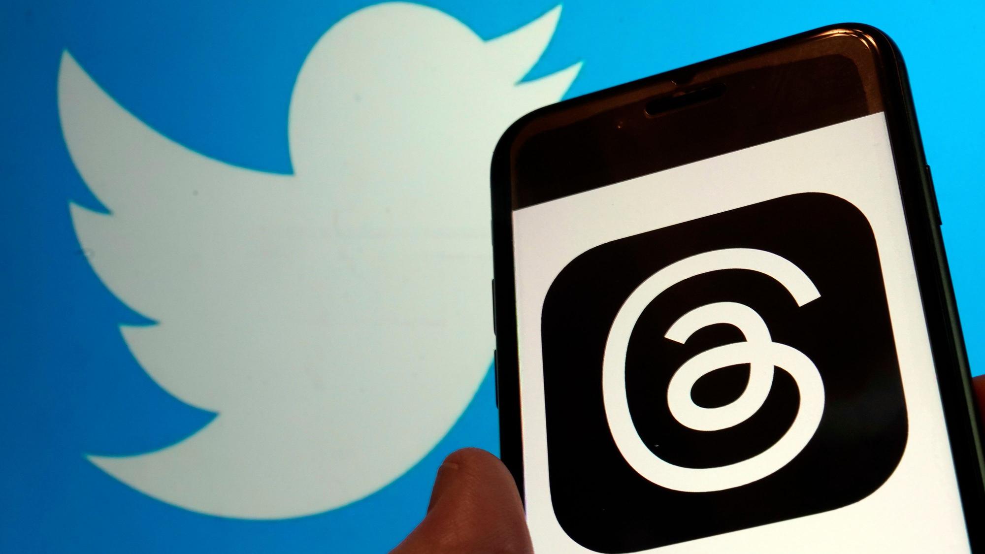 Blick auf das Logo für Metas neue App Threads auf einem Handy-Display und das Logo von Twitter.