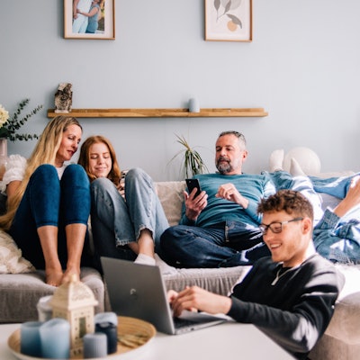 Eine Familie sitzt gemeinsam auf einer Couch. Davor sitzt ein Jugendlicher an einem Laptop.