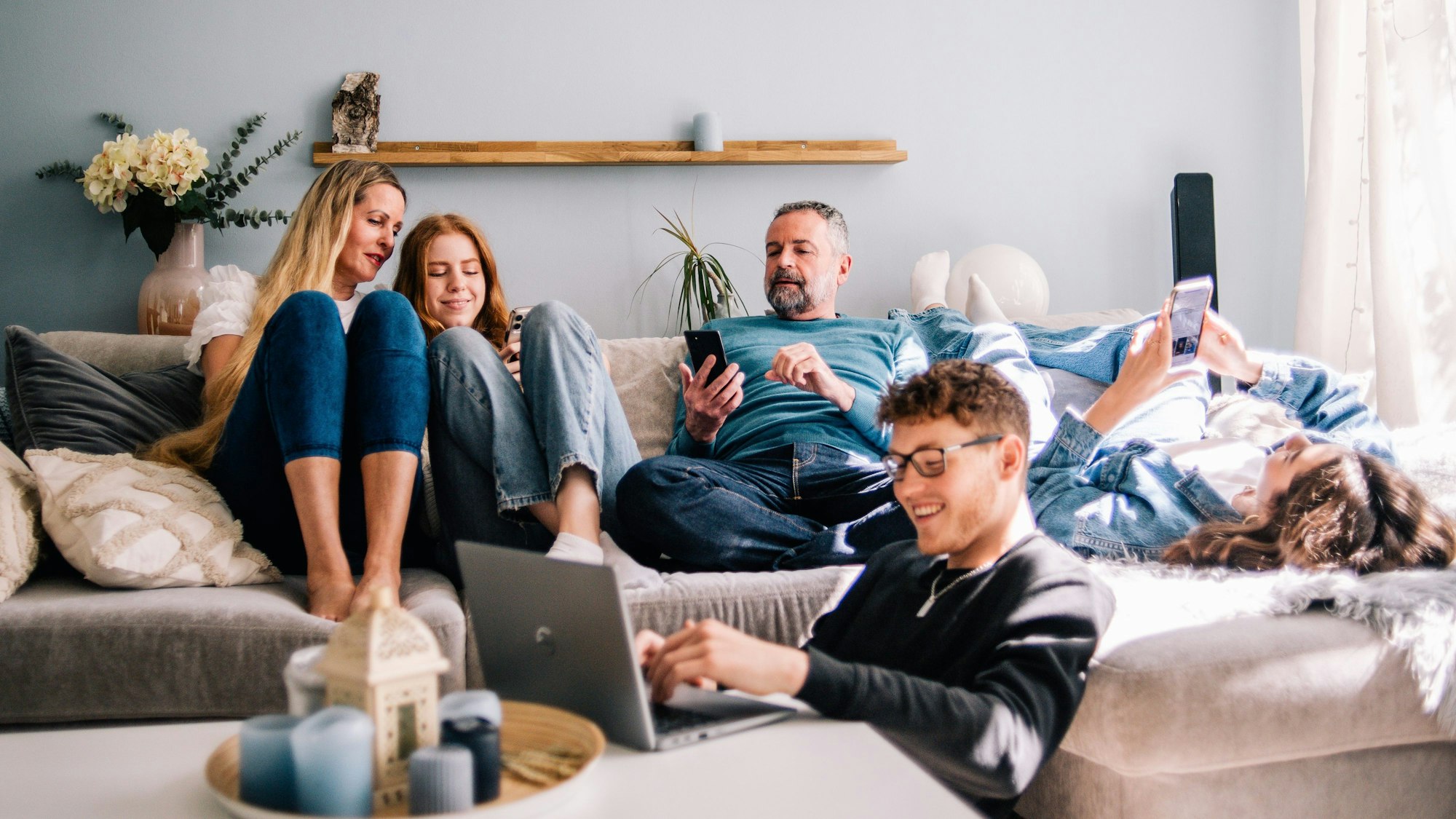 Eine Familie sitzt gemeinsam auf einer Couch. Davor sitzt ein Jugendlicher an einem Laptop.