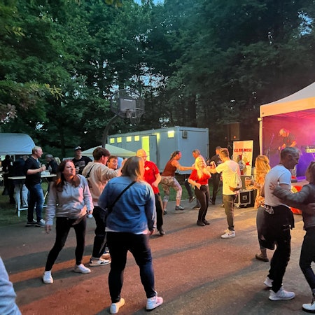 Menschen tanzen auf einem Open-Air-Platz vor einer kleinen Bühne.