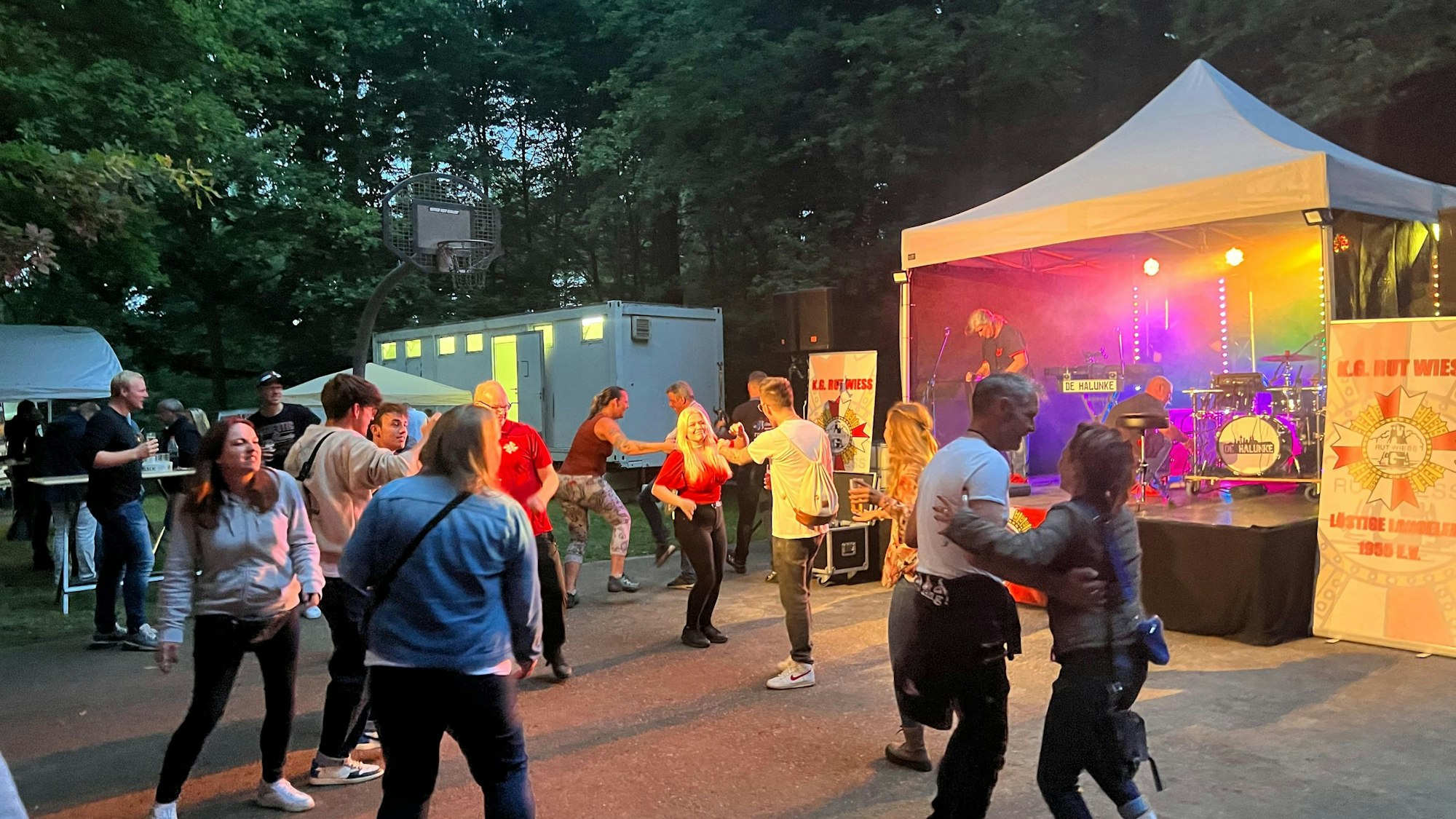 Menschen tanzen auf einem Open-Air-Platz vor einer kleinen Bühne.