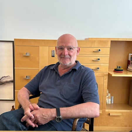 Ein Mann sitzt vor einer Kommode, daneben ist ein Bild mit einer Maus zu sehen.