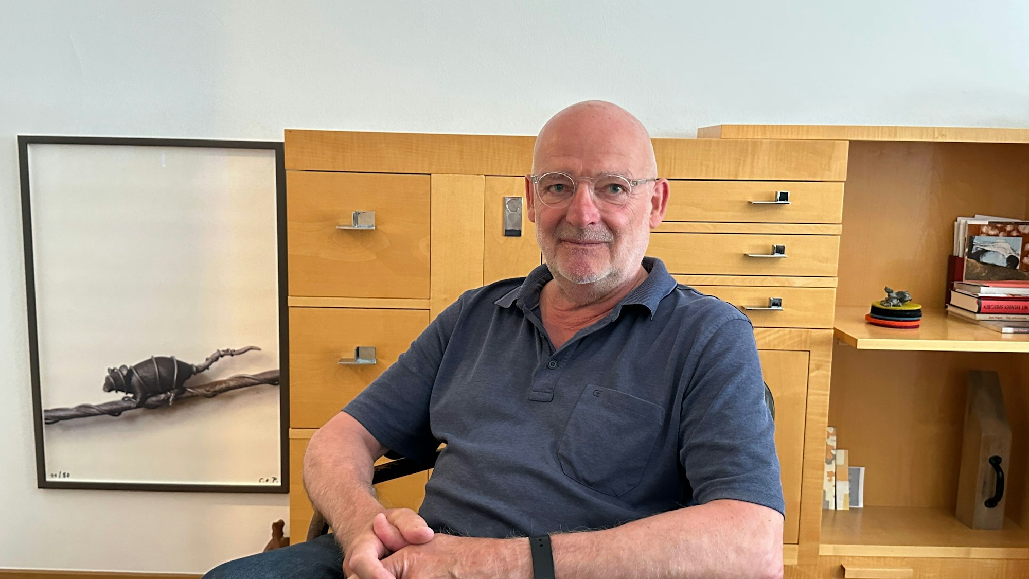 Ein Mann sitzt vor einer Kommode, daneben ist ein Bild mit einer Maus zu sehen.