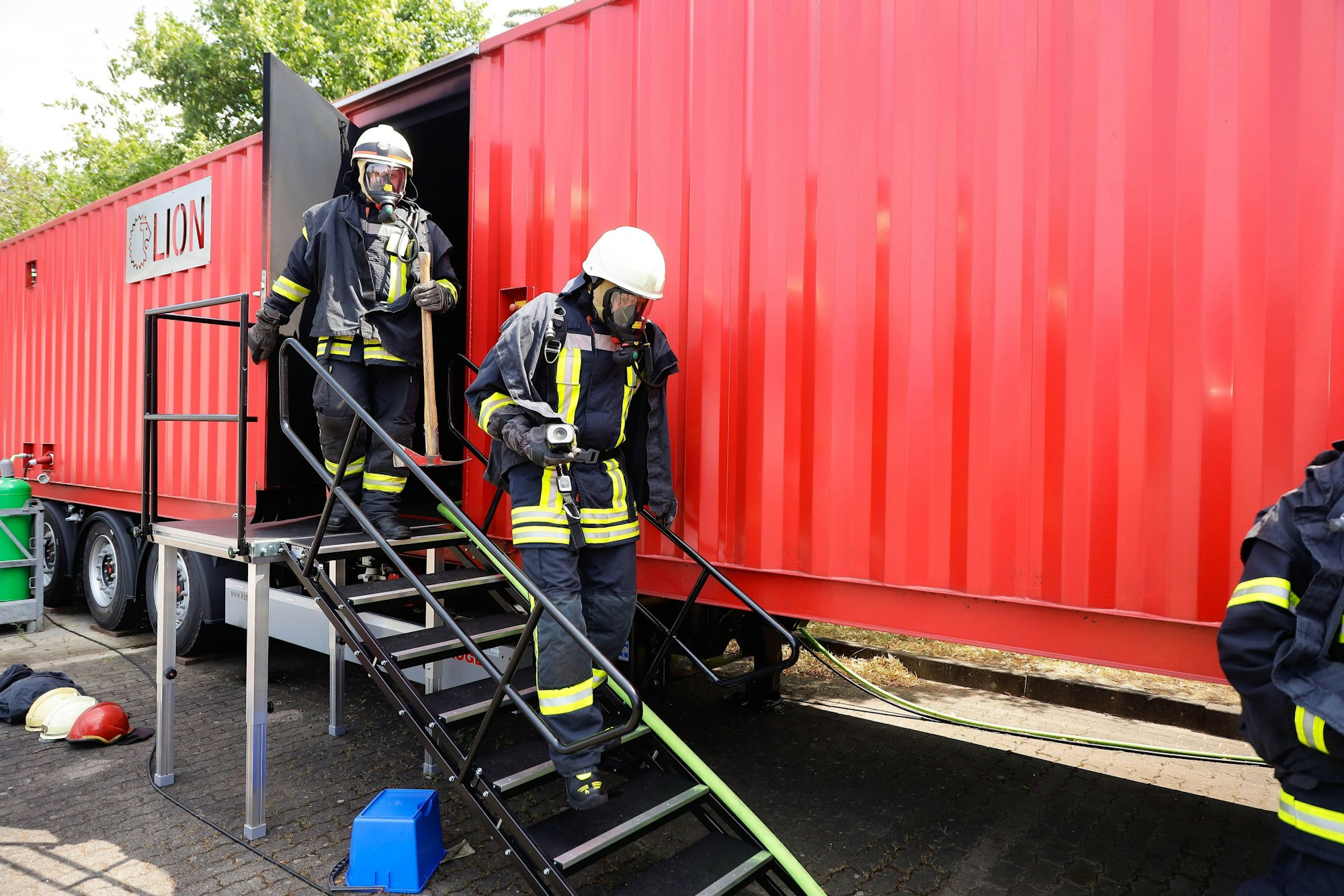 Zwei Männer in Feuerwehruniform verlassen den Brandcontainer über eine Treppe.