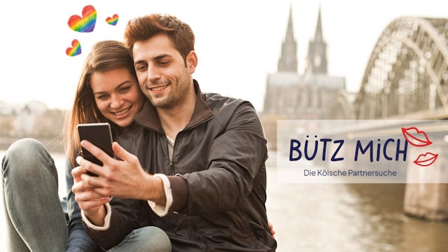Eine Frau und ein Mann stehen auf der Rheinpromenade mit dem Kölner Dom und der Hohenzollernbrücke im Hintergrund und schauen lächelnd auf ein Smartphone. Daneben das Logo der Website Bütz mich.
