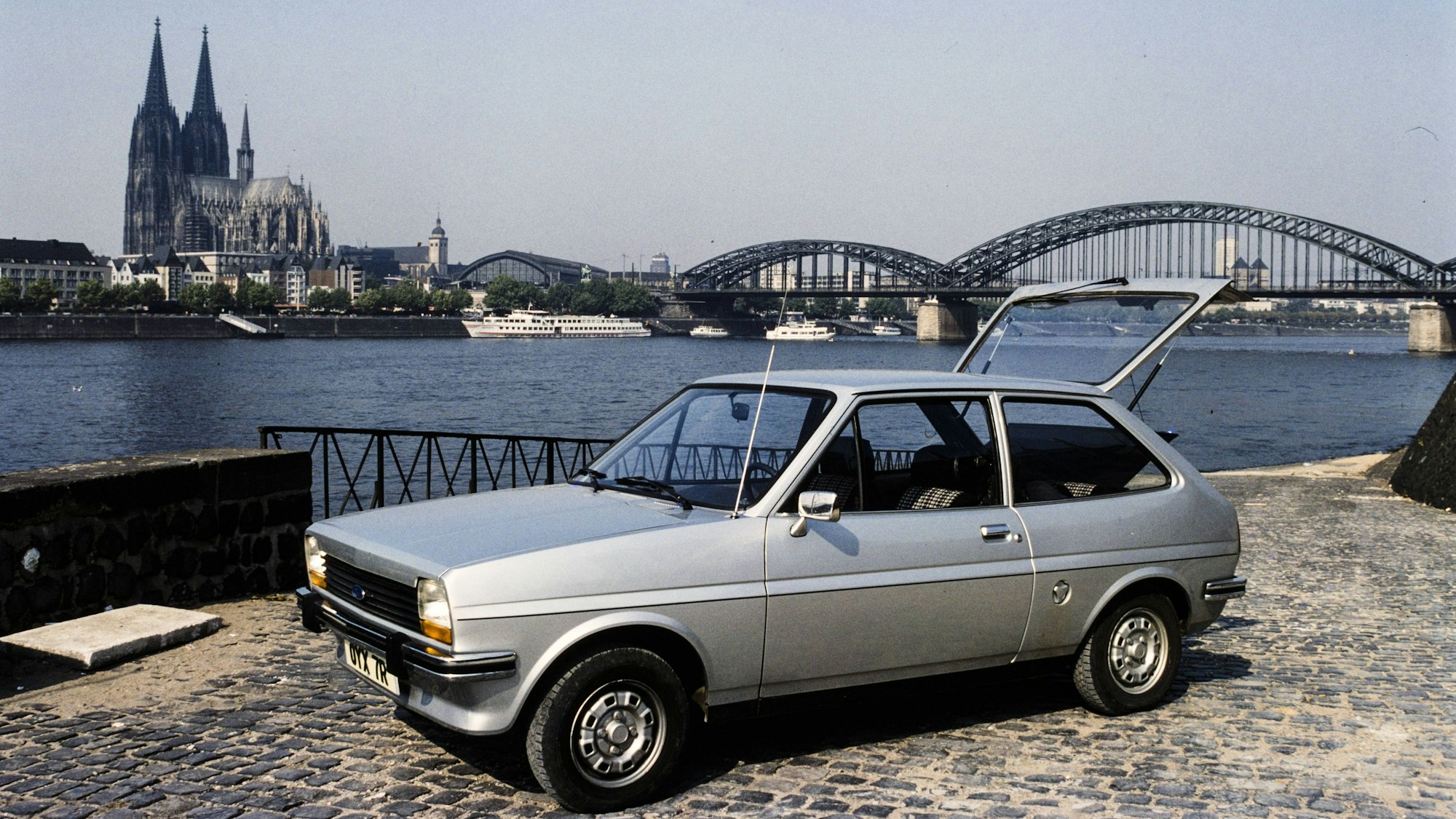 Ein silberner Ford Fiesta am Rhein mit dem Kölner Dom und der Hohenzollernbrücke im Hintergrund.