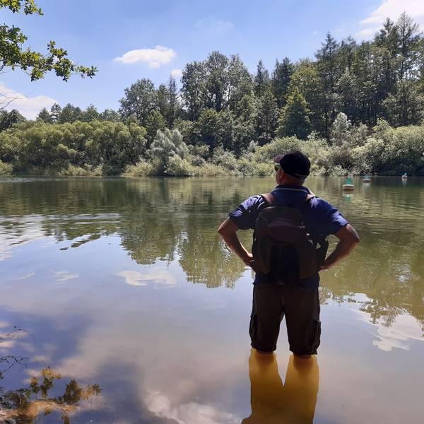 Ein Wanderer steht bis zu den Knien im Wasser am Ufer eines Stausees.