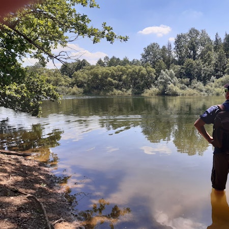 Ein Wanderer steht bis zu den Knien im Wasser am Ufer eines Stausees.