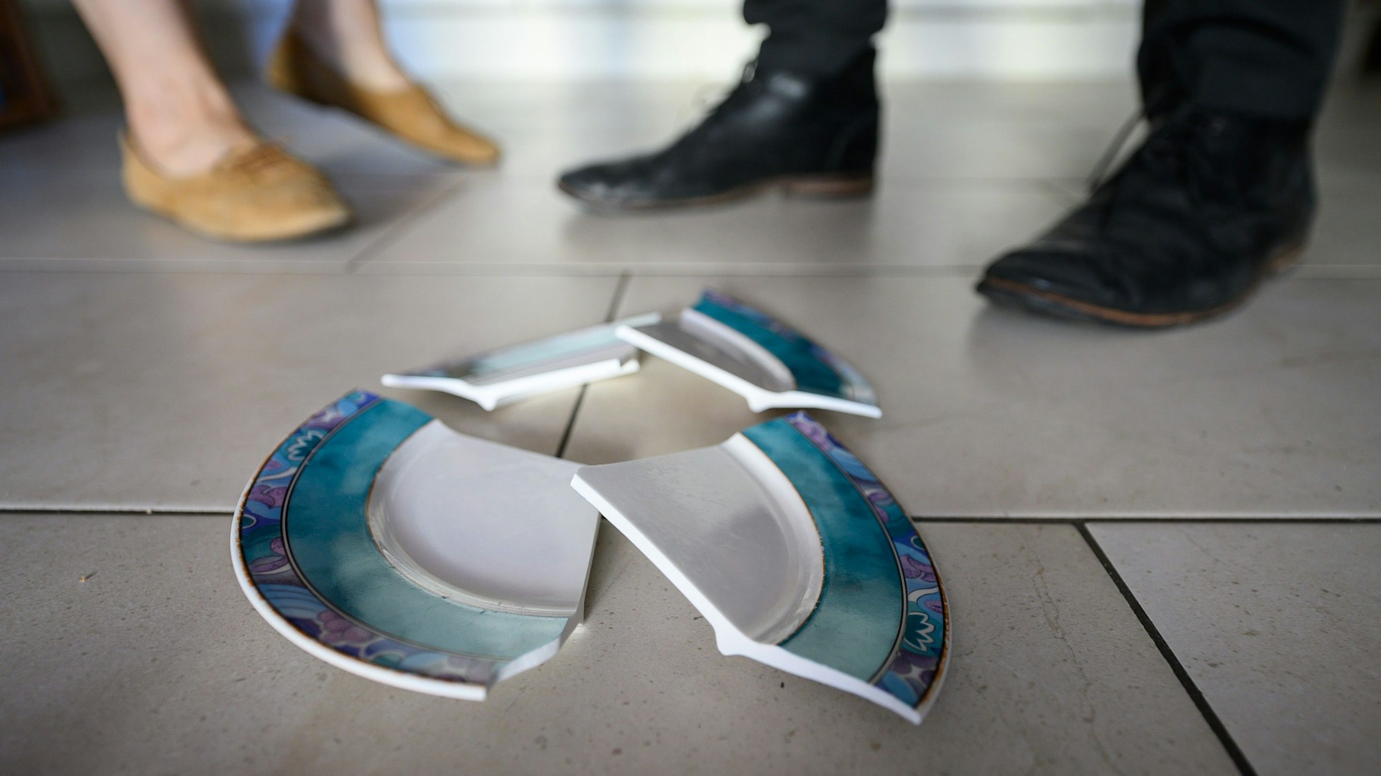 Ein Mann und eine Frau stehen sich hinter einem zerbrochenen Teller in einer Küche gegenüber