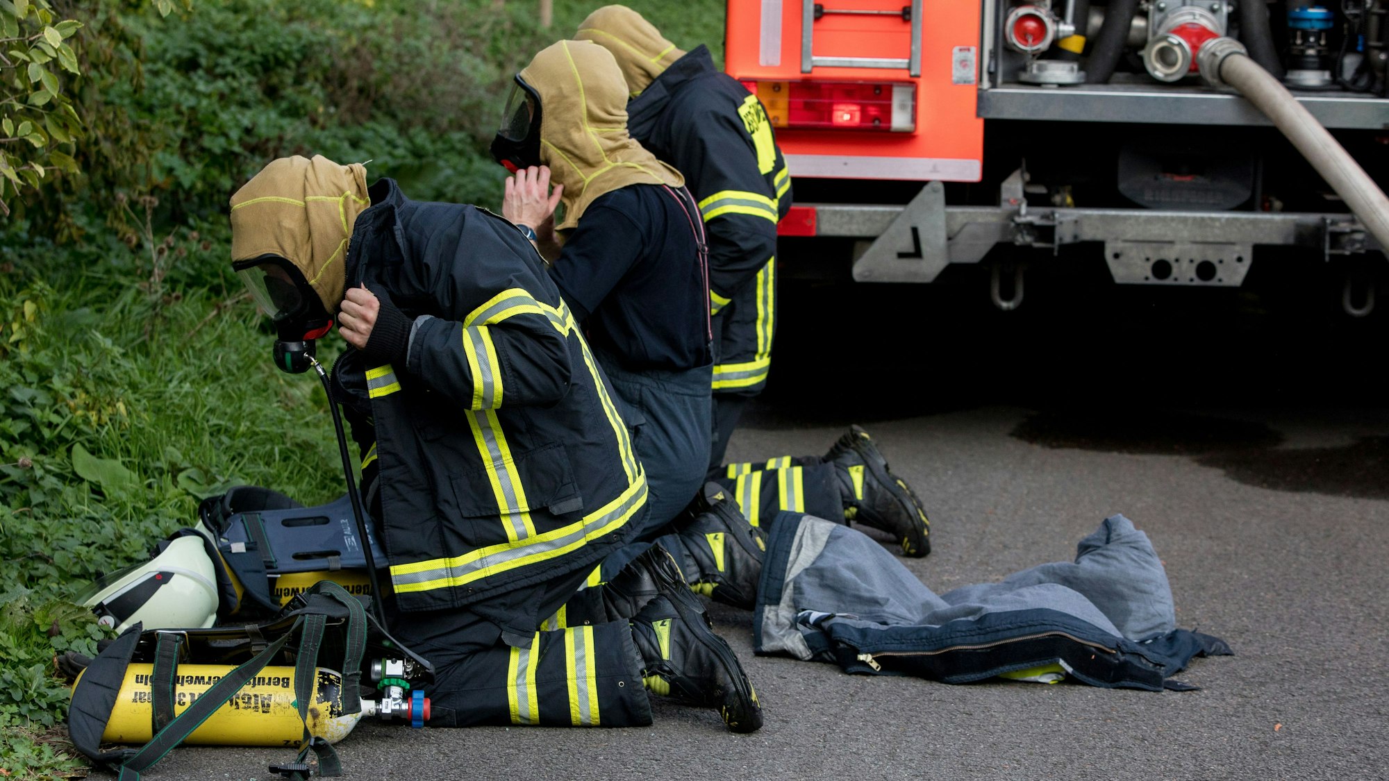 Drei Feuerwehrleute knien auf dem Boden und tragen Atemschutzmasken.