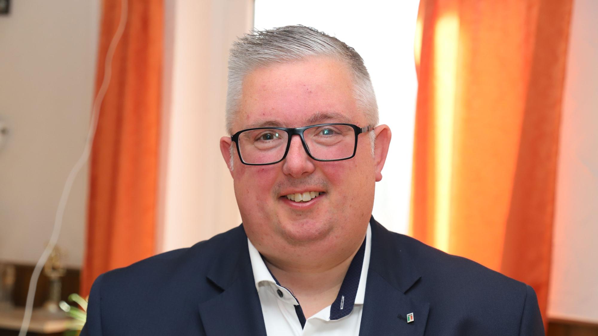 Sascha Lienesch trägt einen Anzug und ein weißes Hemd und lächelt in die Kamera.