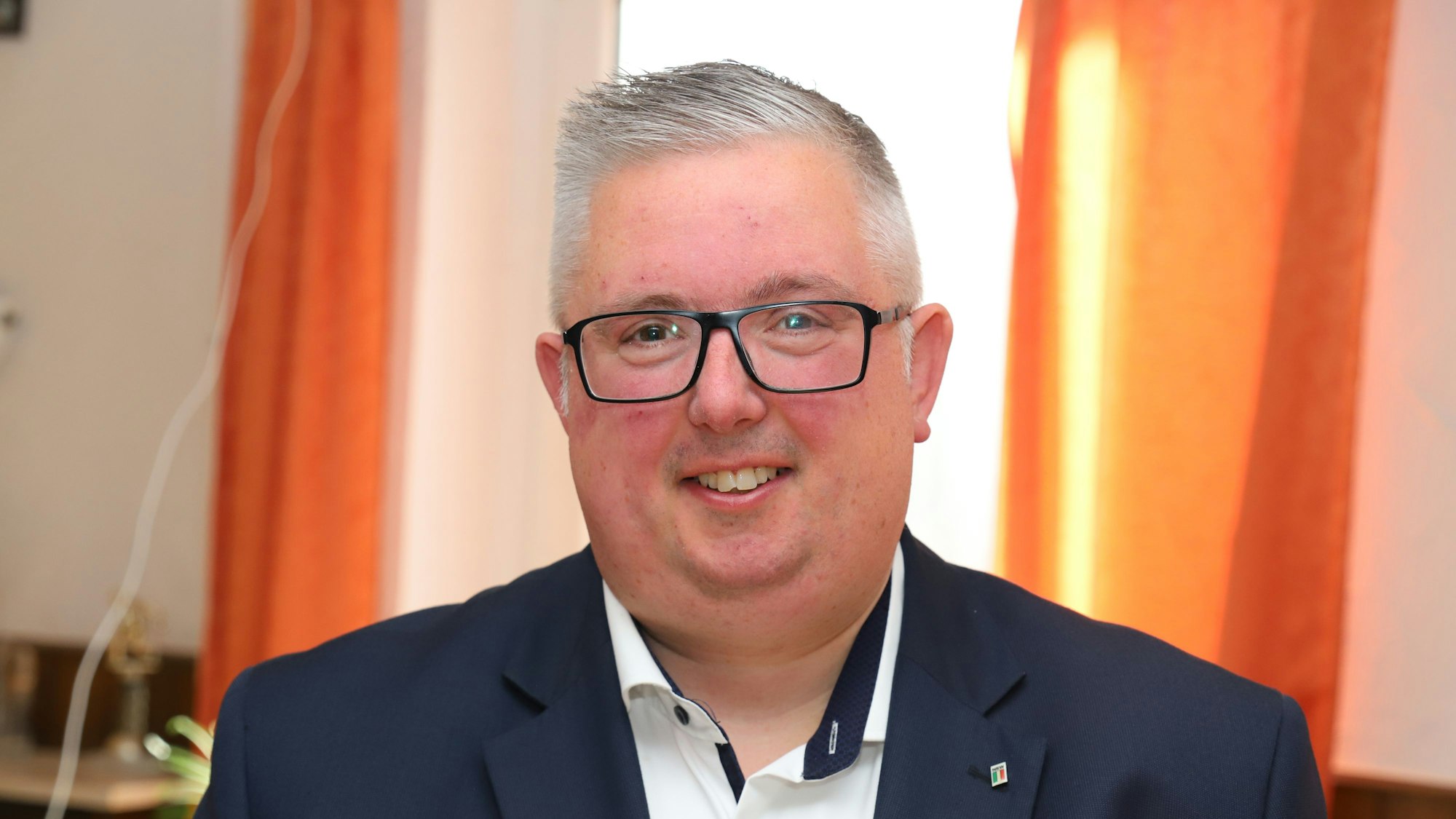 Sascha Lienesch trägt einen Anzug und ein weißes Hemd und lächelt in die Kamera.