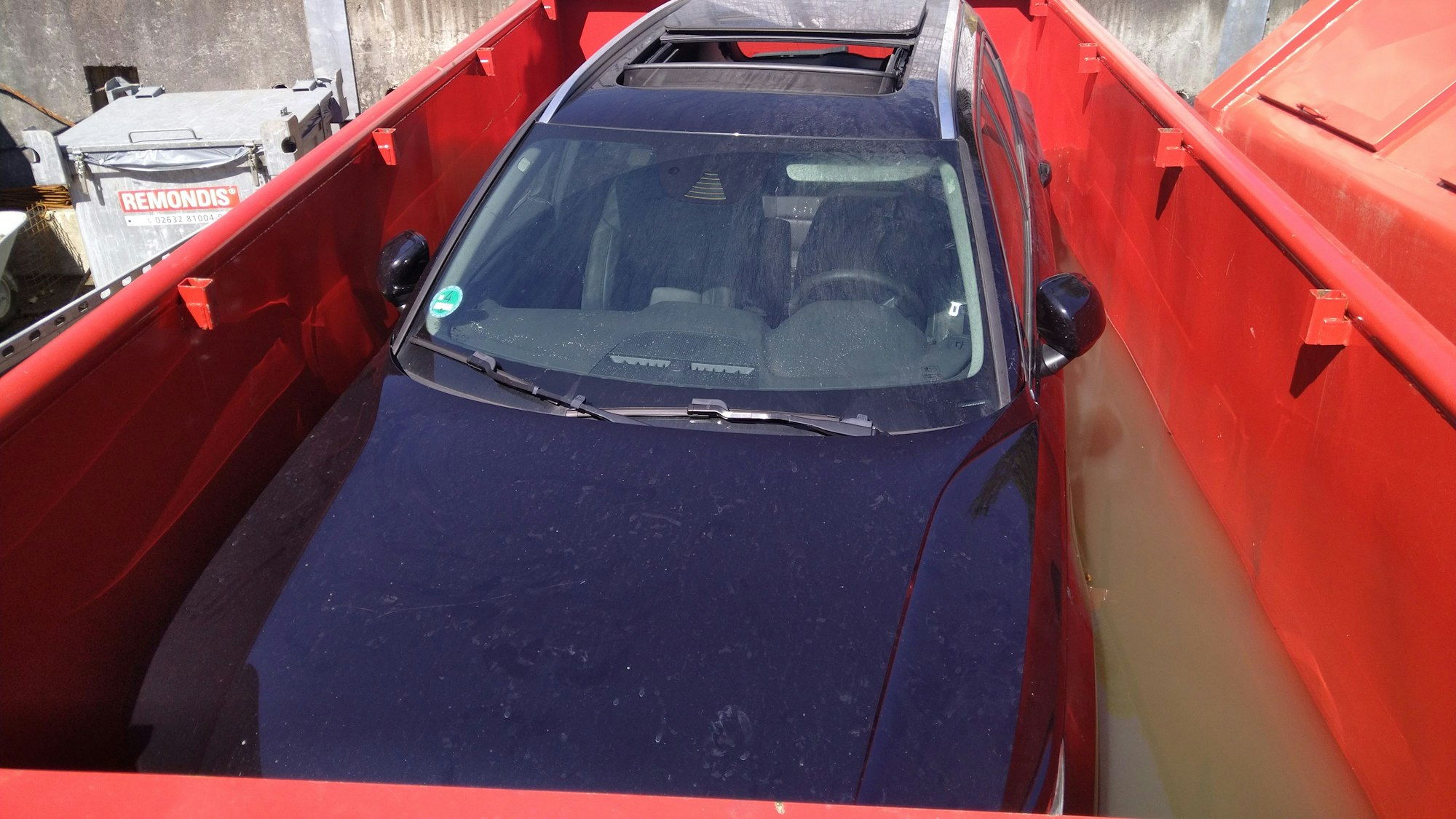 Das E-Auto steht in einem Spezailconteiner der mit einer Flüssigkeit gefüllt ist.