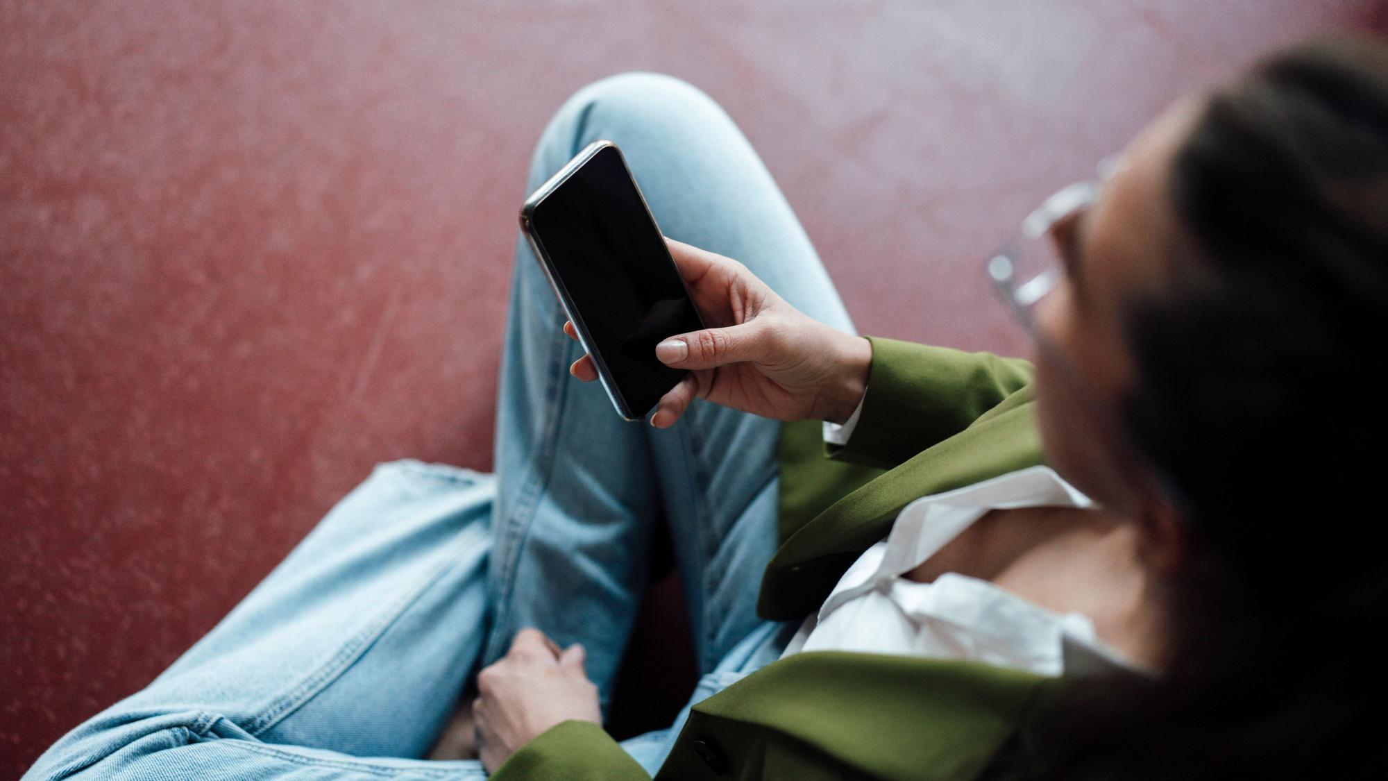 Eine junge Frau hält ein Smartphone in der Hand.