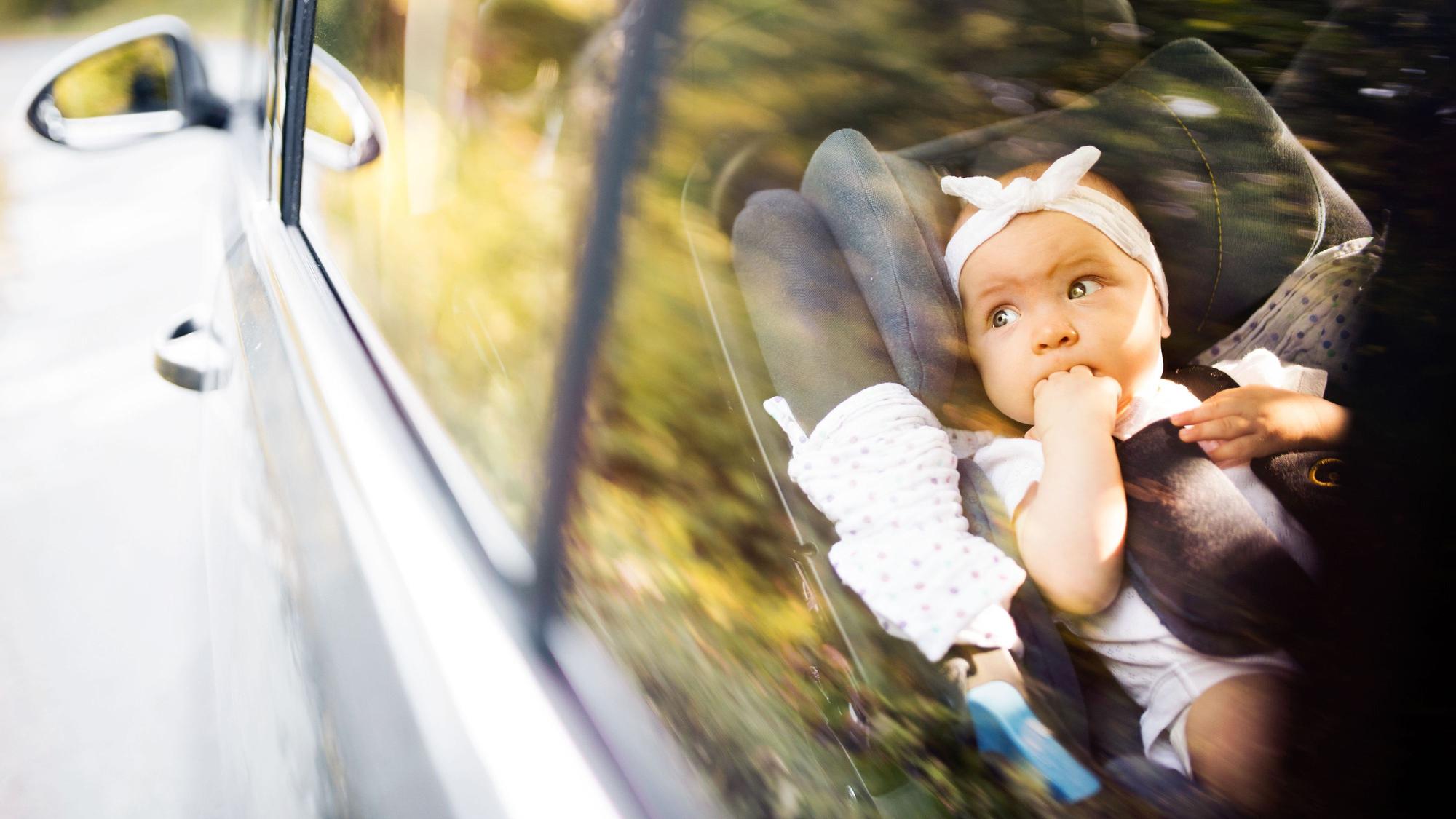 Niedliches kleines Mädchen, das mit einem Sicherheitsgurt im Autositz befestigt ist. Durch Glas geschossen.