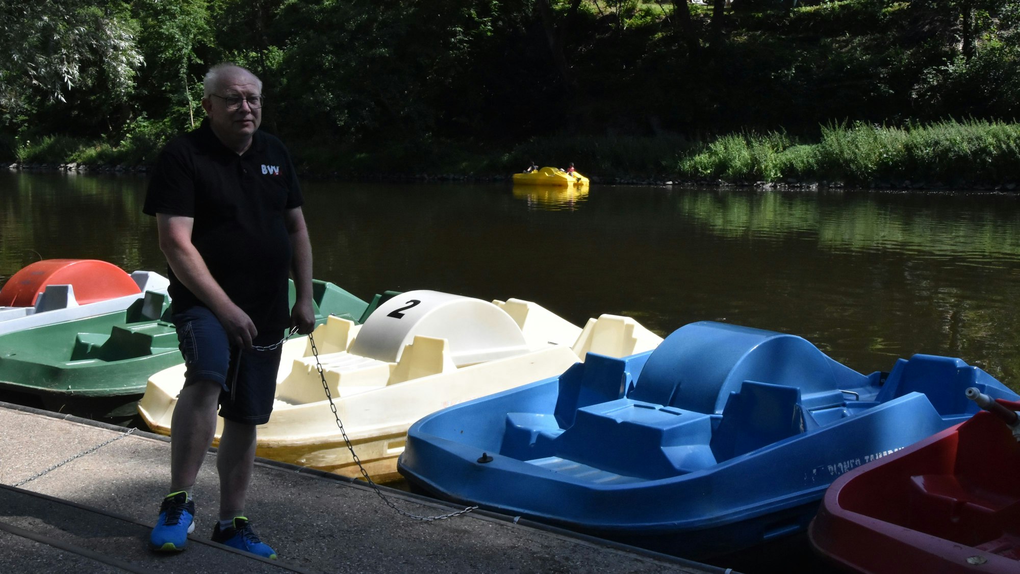 Ein Mann steht an einer Anlegestelle mit Tretbooten.