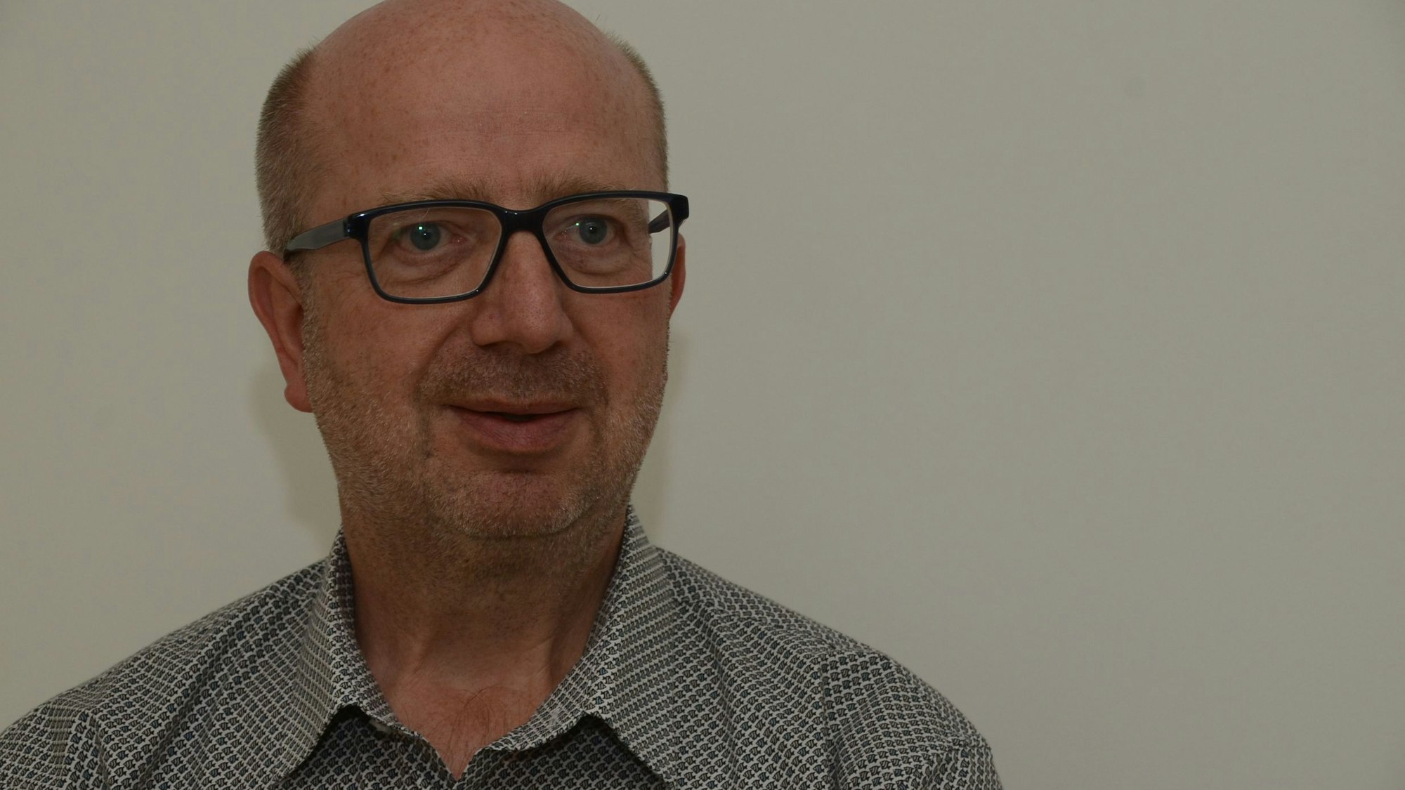 Ein Mann mit gemustertem Hemd und einer Brille mit schwarzem Rand.