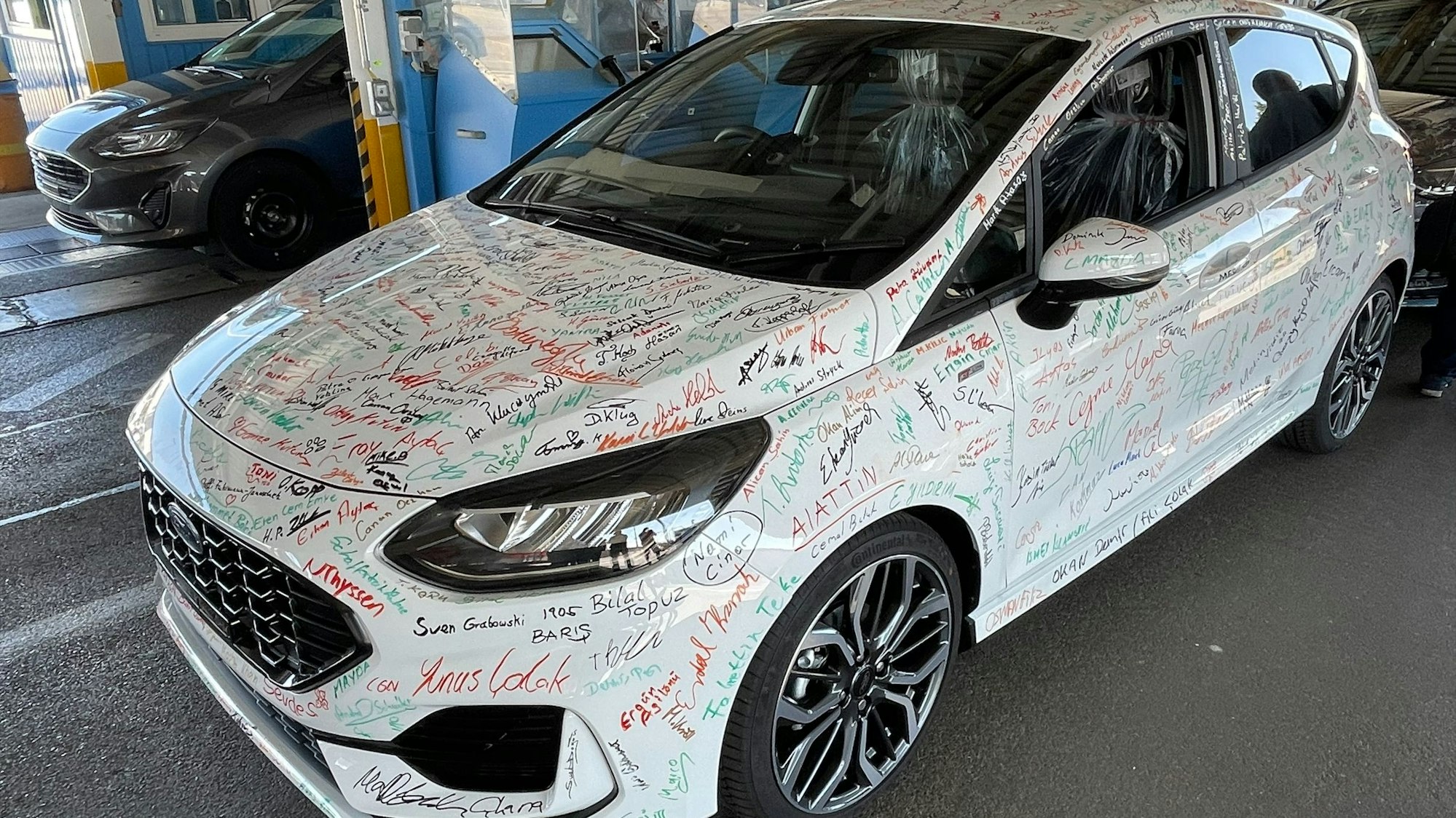 Mitarbeiterinnen und Mitarbeiter signieren die letzten Ford Fiestas.