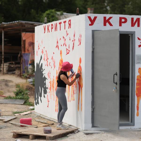 Eine Künstlerin zeichnet orangefarbene Figuren auf die weißen Wände des Bunkers.