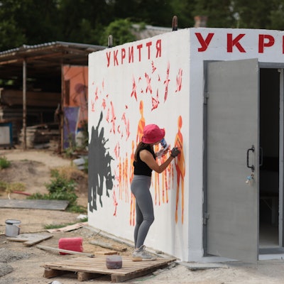 Eine Künstlerin zeichnet orangefarbene Figuren auf die weißen Wände des Bunkers.