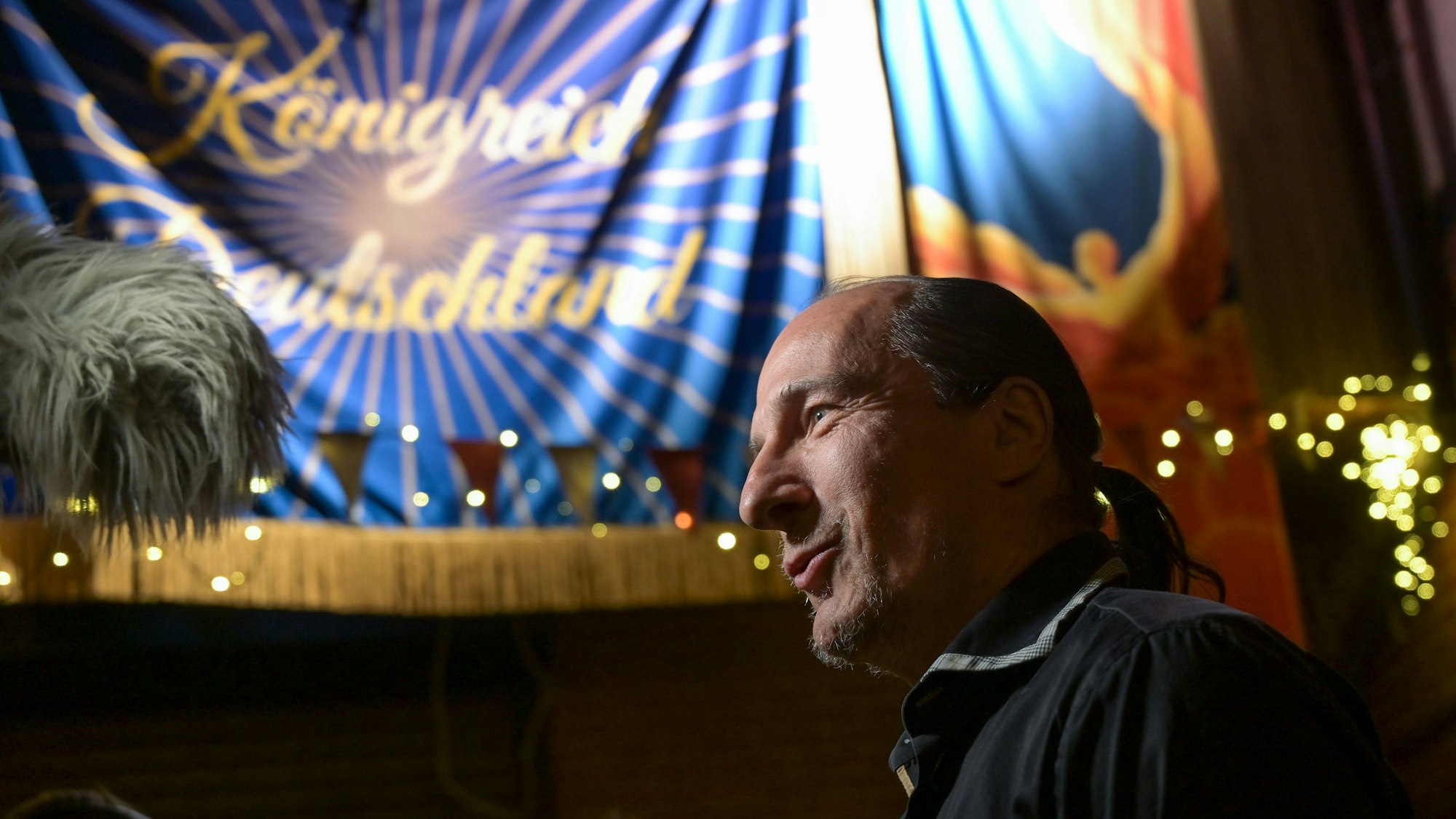 Peter Fitzek, selbsternannter Oberster Souverän und „König von Deutschland“, im Seitenporträt. Im Hintergrund sieht man ein Banner mit der Aufschrift „Königreich Deutschland“.