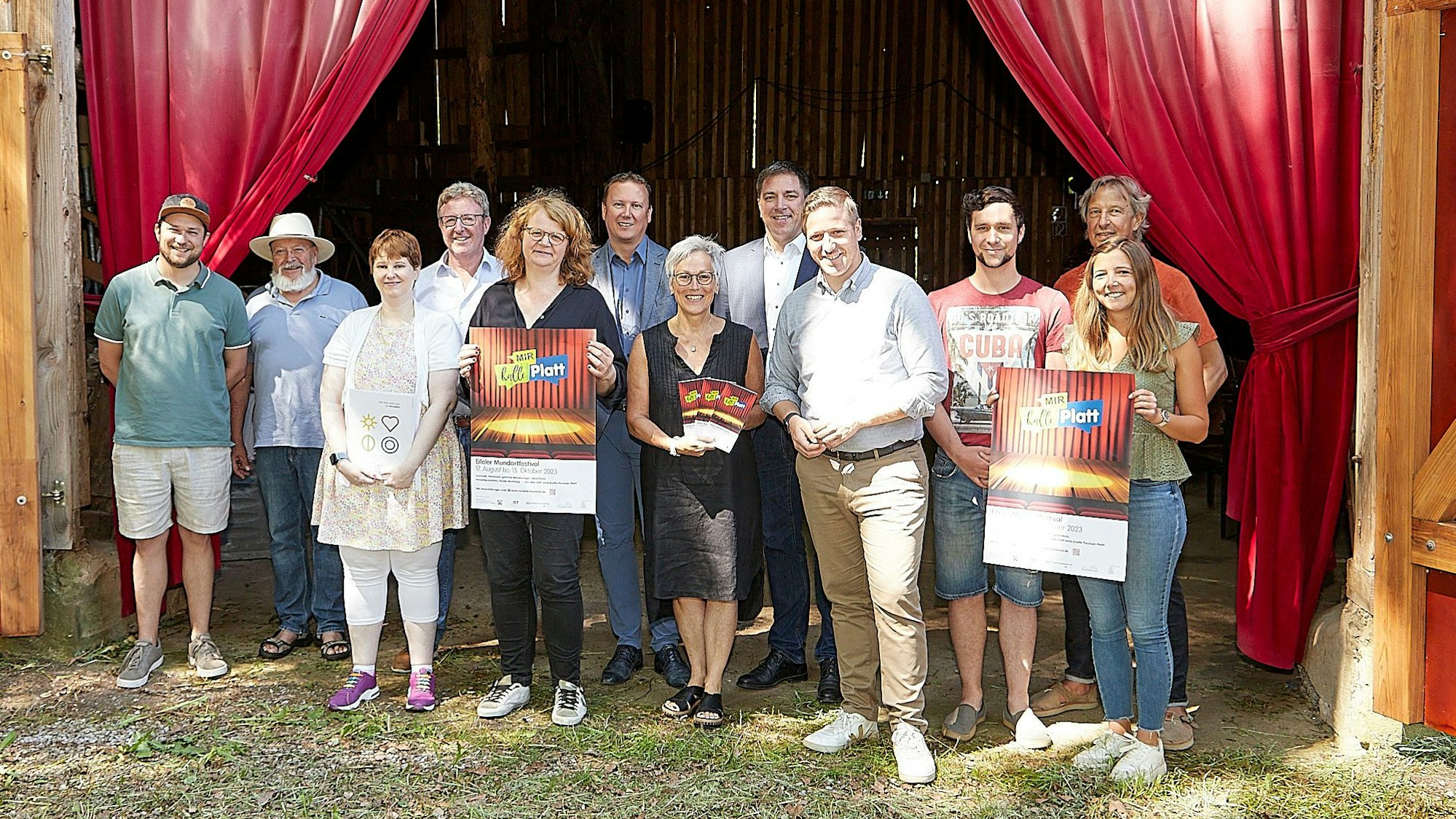Eine Gruppe von Menschen steht vor einem roten Theatervorhang, einige halten Plakate in den Händen.