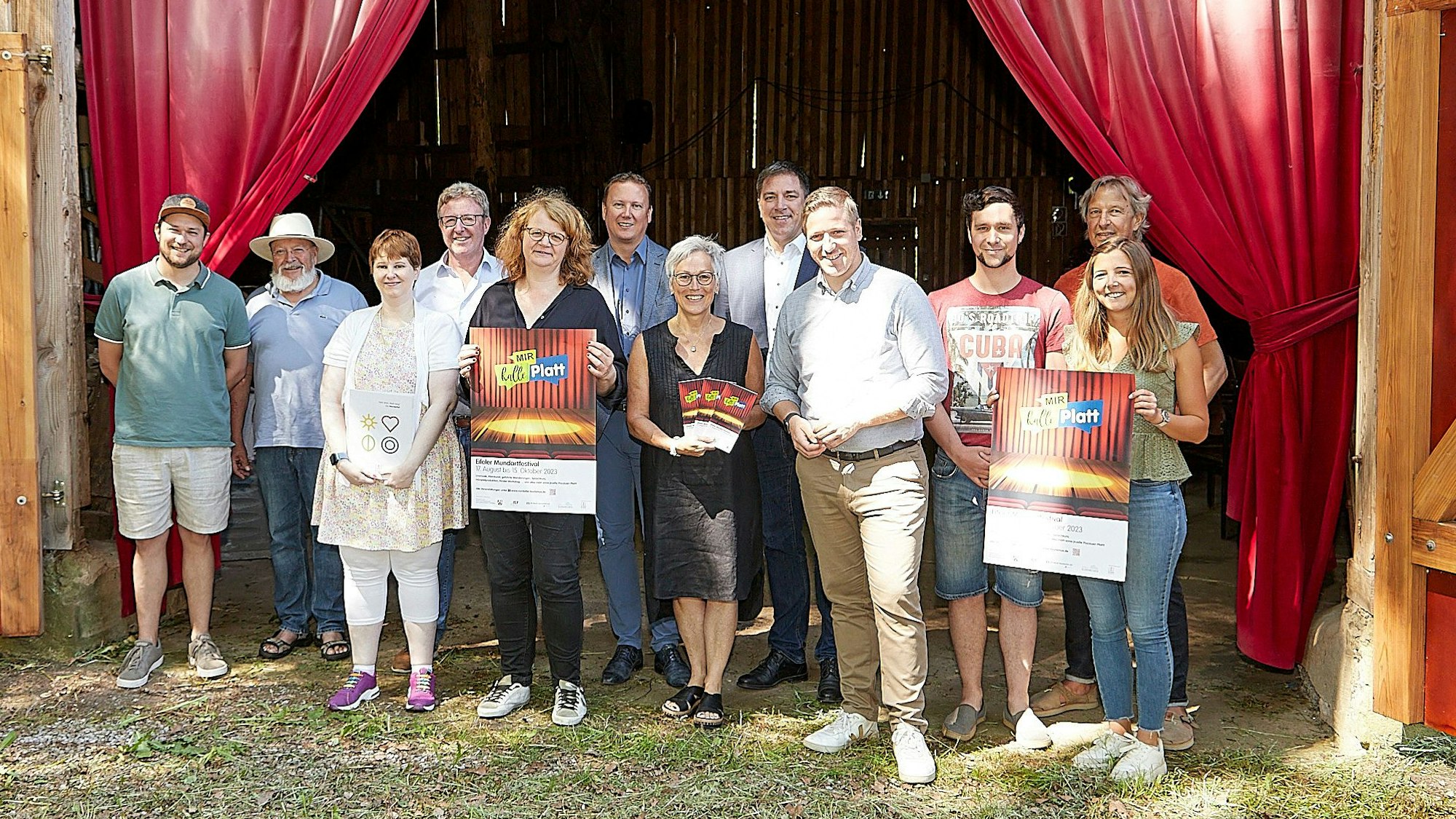 Eine Gruppe von Menschen steht vor einem roten Theatervorhang, einige halten Plakate in den Händen.