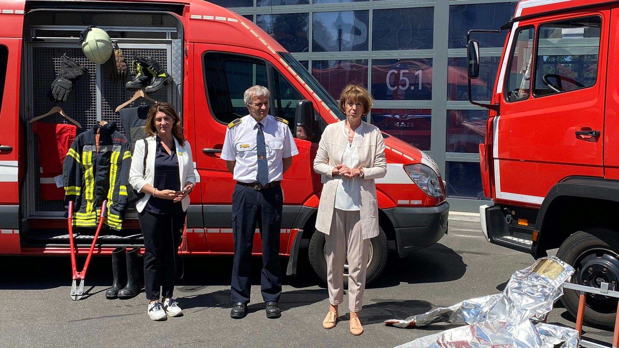 Auf dem Bild stehen drei Personen vor zwei roten Feuerwehrfahrzeugen.
