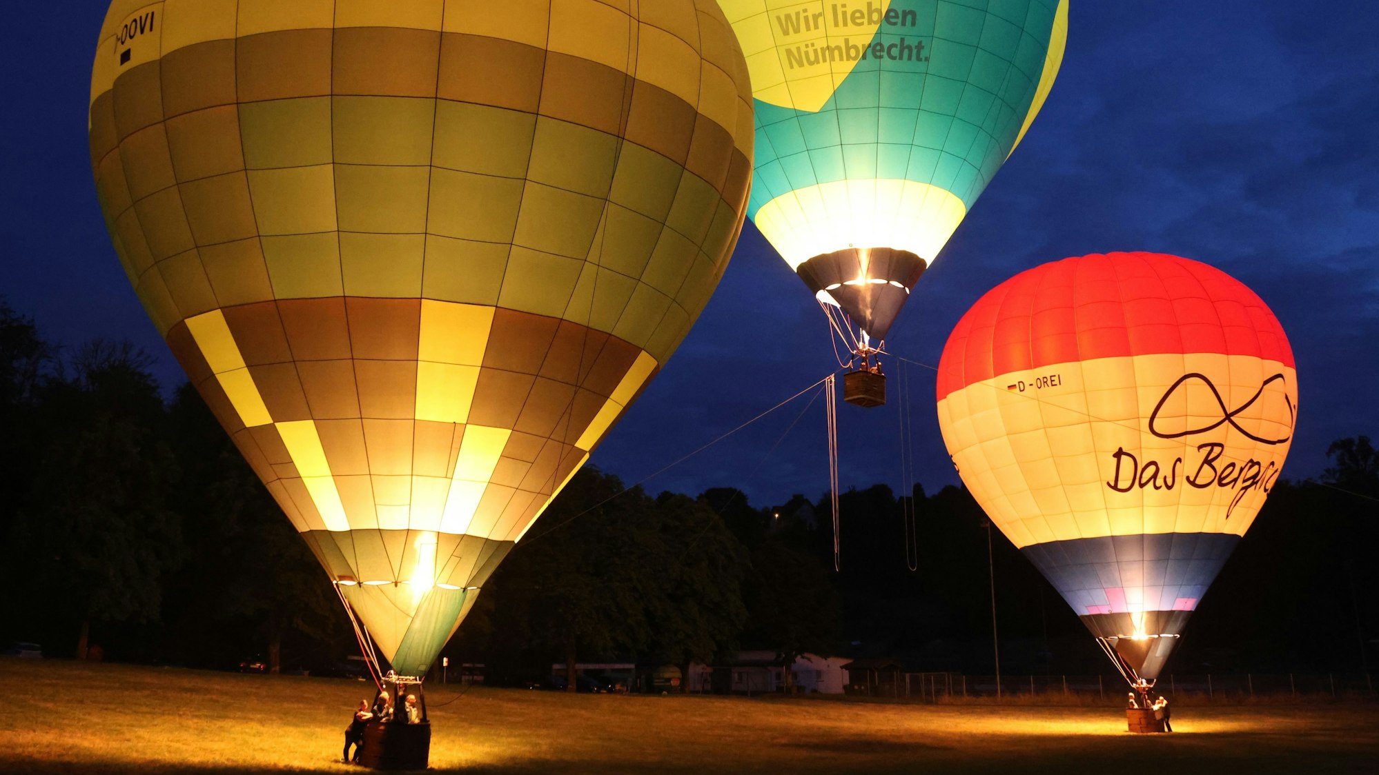 Drei Heißluftballone glühen in der Dunkelheit.