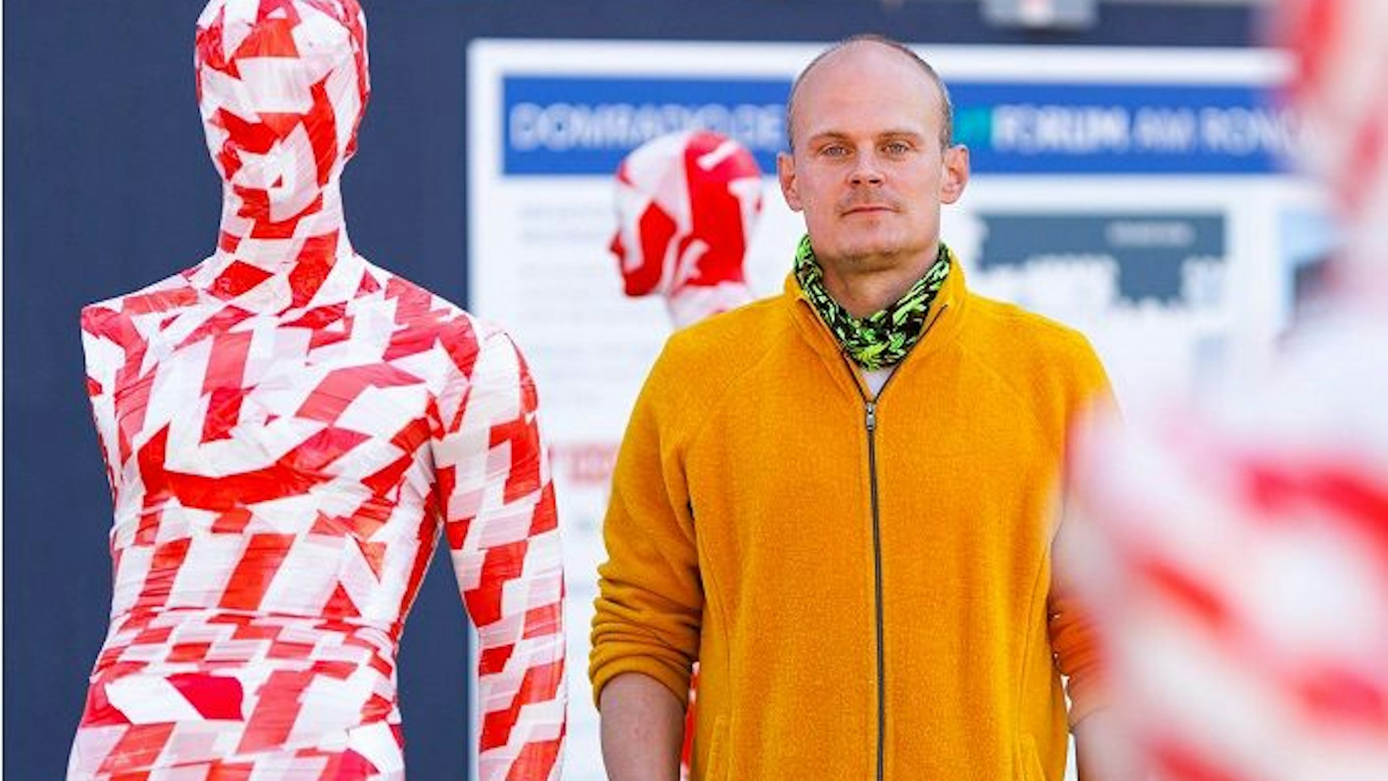 Das Foto zeigt den Künstler vor einer von 222 Schaufensterpuppen. Sie ist komplett mit rot-weißem Band umwickelt.