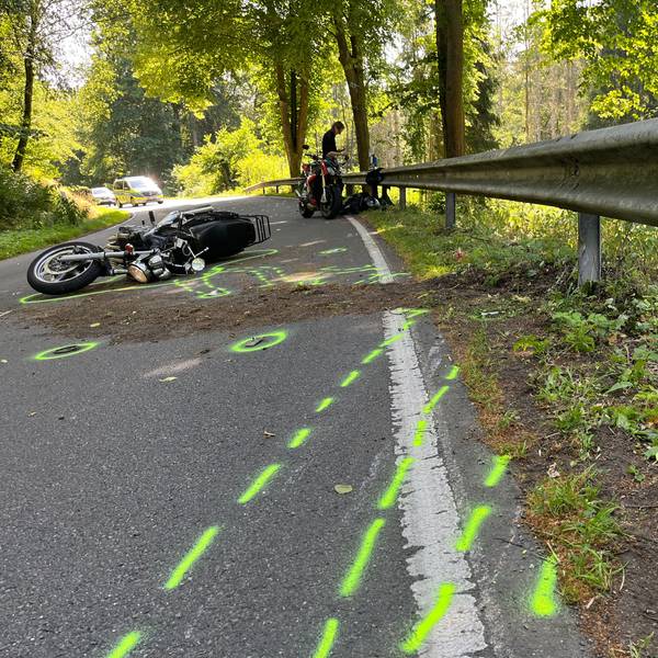 Ein Motorrad liegt nach einem Zusammenstoß auf dem Boden. Vor dem Zweirad wurden von der Polizei Unfallmarkierungen auf den Boden gesprüht.