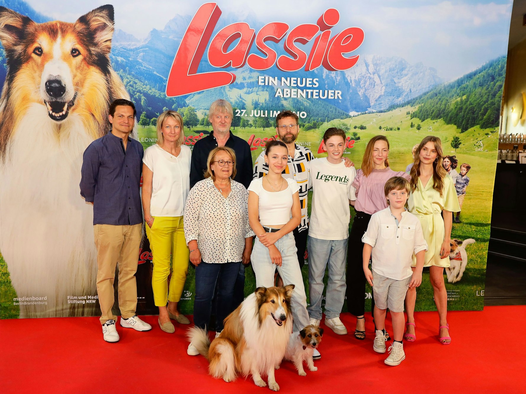 Mehrere Menschen und zwei Hunde auf dem Roten Teppich vor einem Filmplakat zu Lassie.